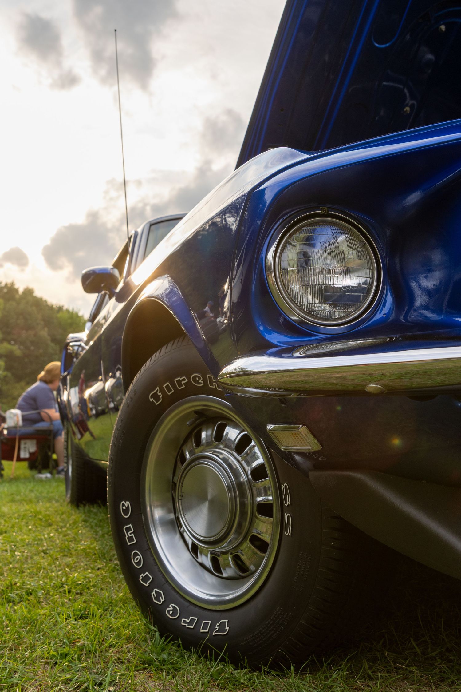 Close-up shots of a classic blue car with vintage Goodyear tires against a dramatic cloudy sky.