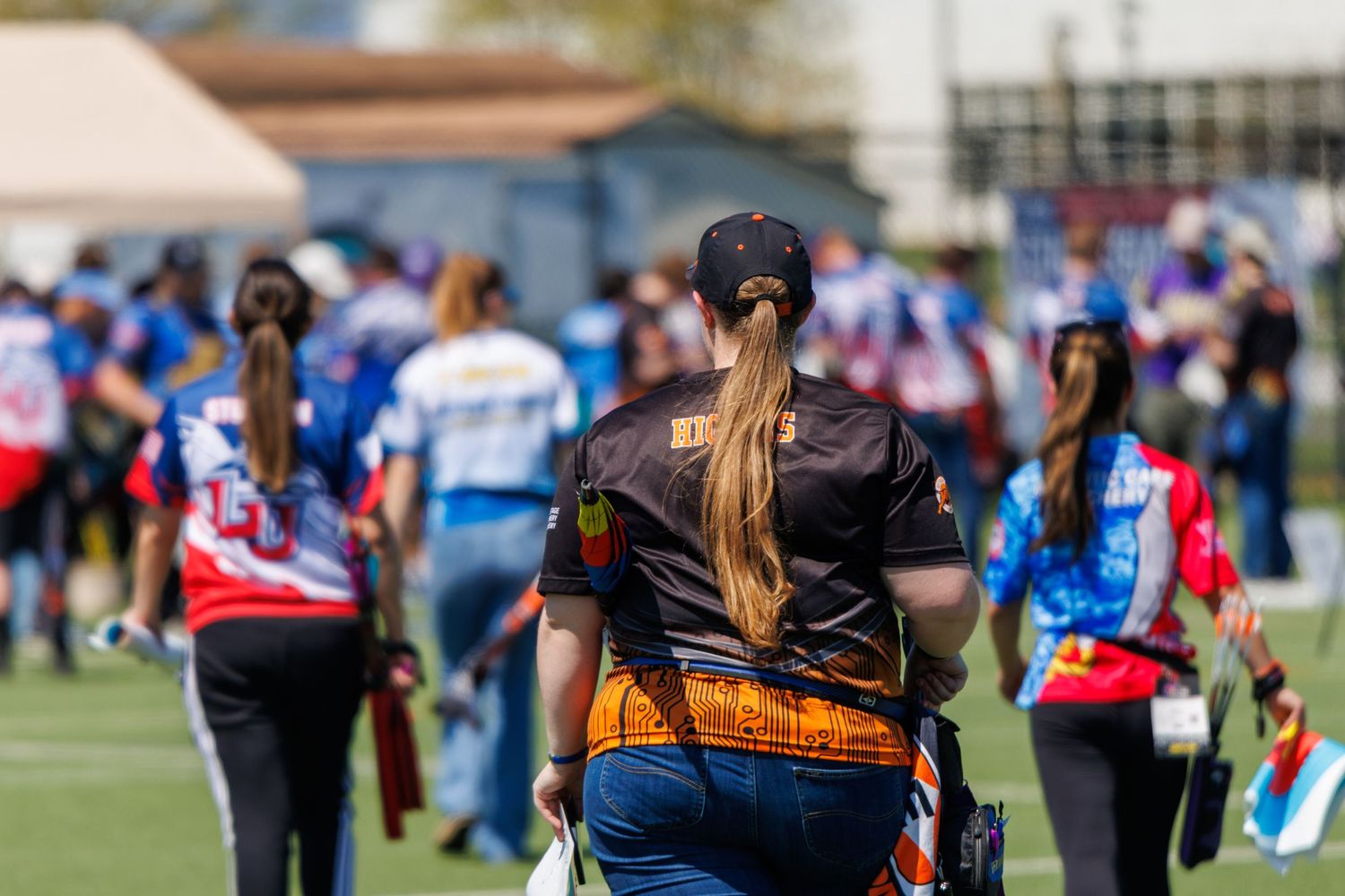 Archers walking across a competition field wearing colorful jerseys at an outdoor archery event.