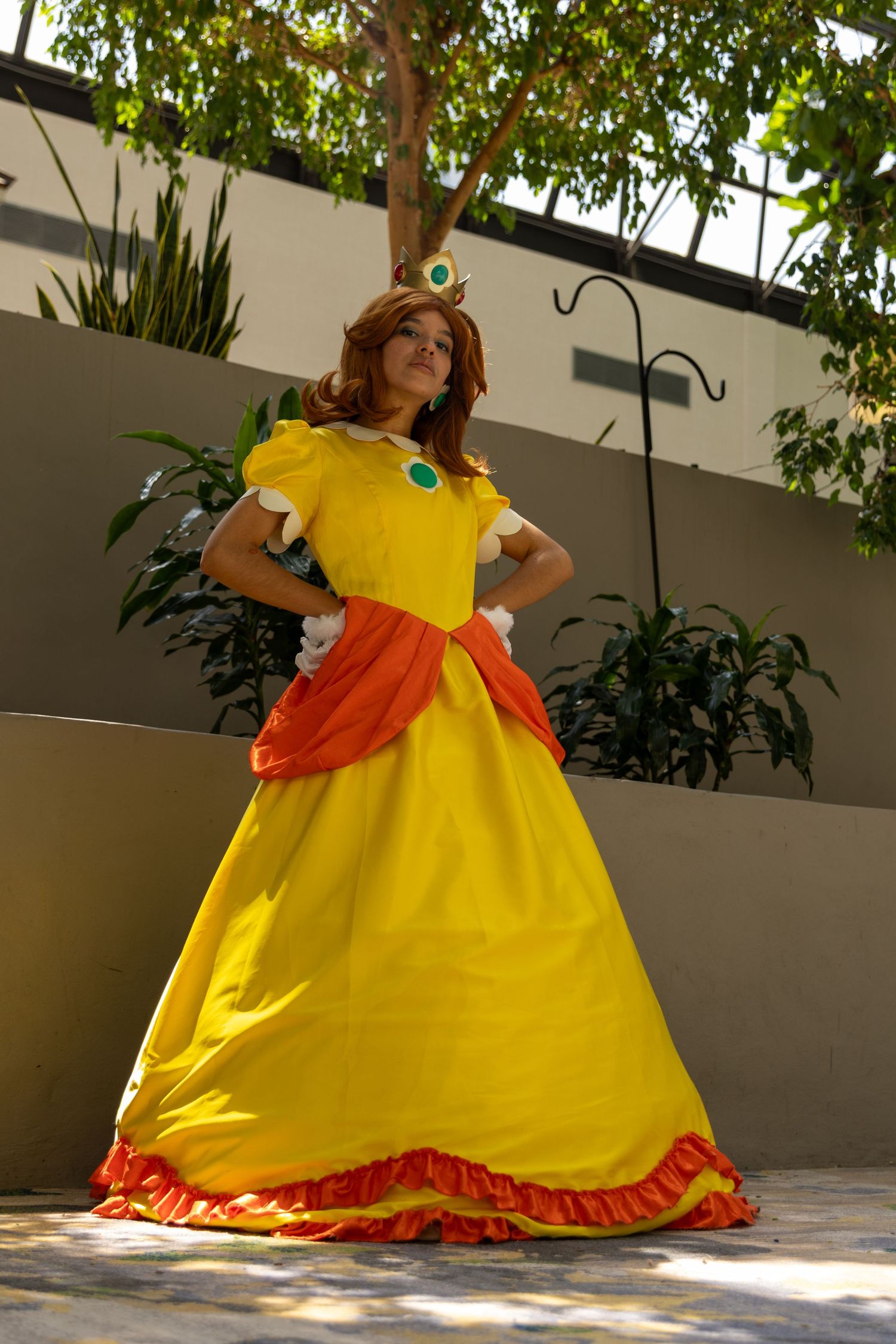 Person twirls in a vibrant yellow and orange princess-style ballgown with puffed sleeves in a sunlit courtyard.
