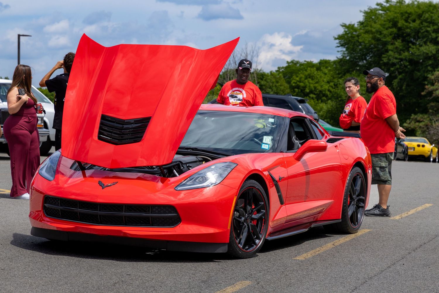 A line of bright red Chevrolet Corvette C7 sports cars parked in a row at an outdoor car meet.
