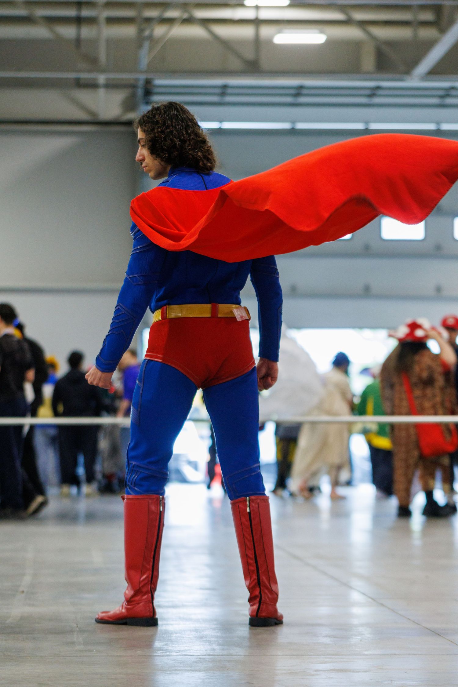 Person cosplaying as Superman with red cape, blue suit, and red boots at a comic convention.