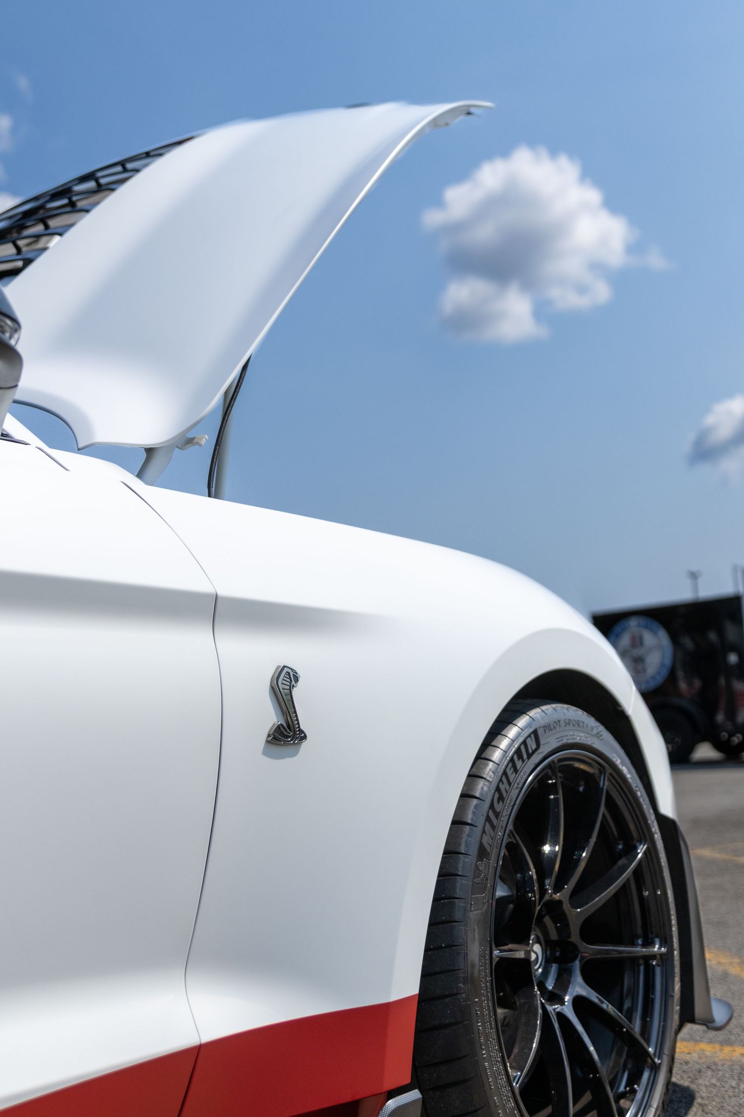 Five cropped closeup detail shots of a white sports car body panels and black wheel against a blue sky background.