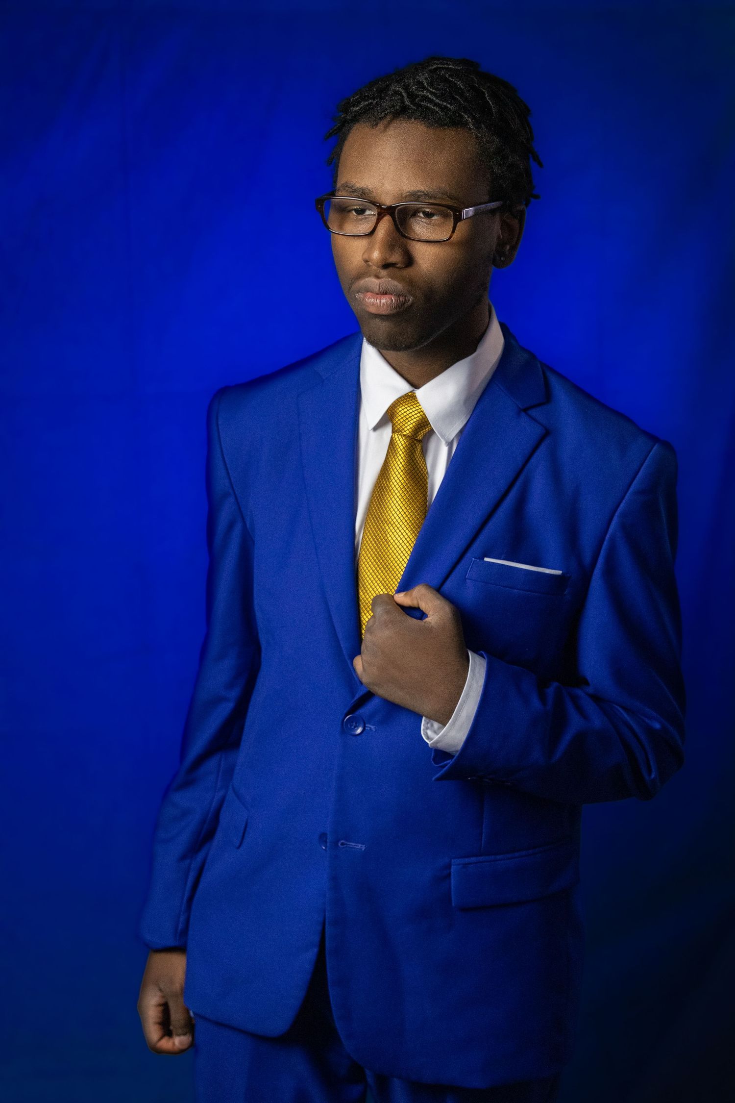 Professional portrait in a royal blue suit with yellow tie against blue background.