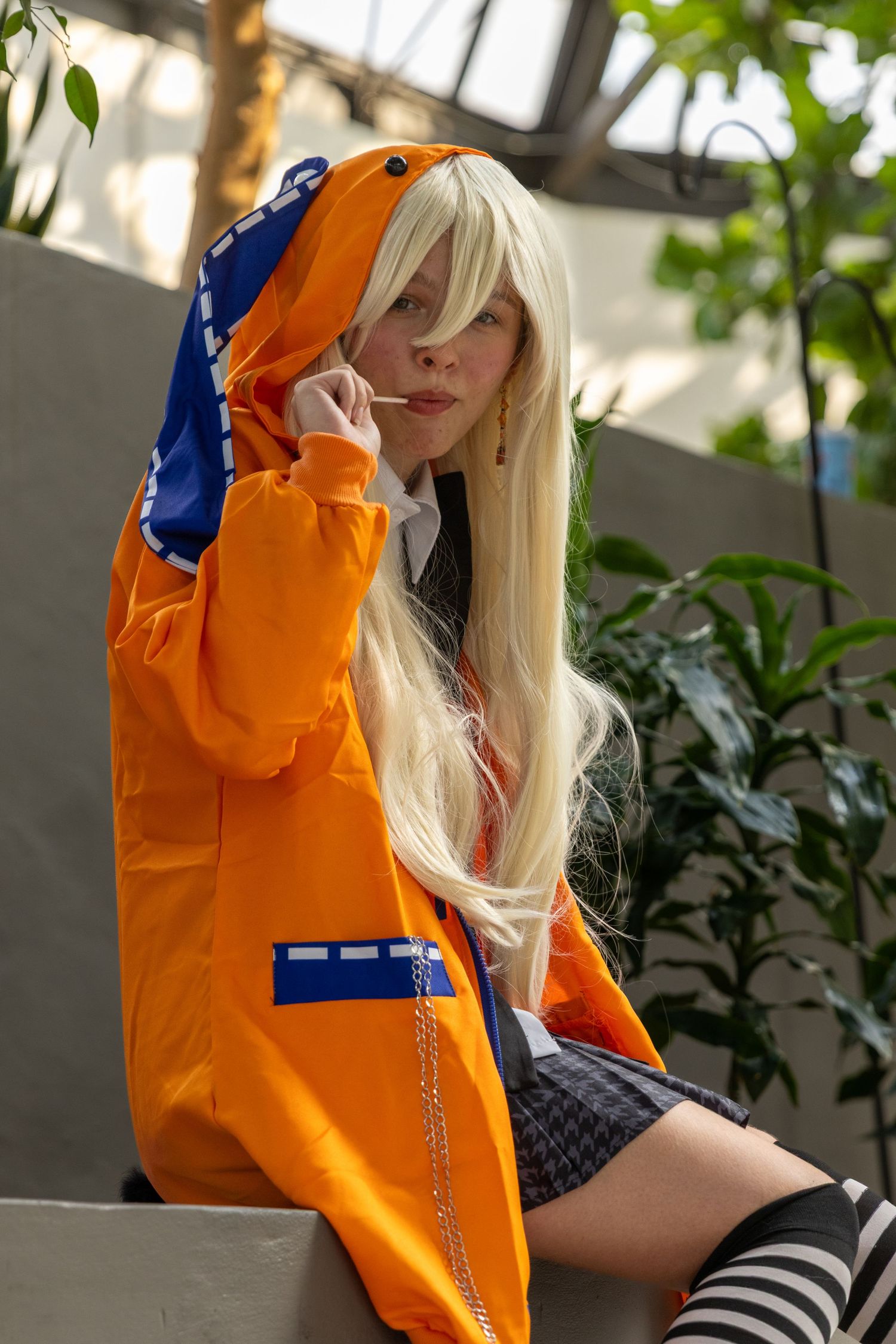 Person in bright orange jacket with blonde hair poses stylishly against greenery background.