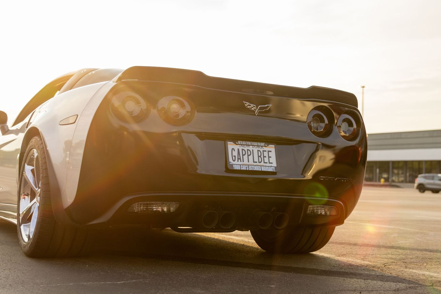 A black Chevrolet Corvette's rear view photographed at sunset with dramatic lighting and shadows.
