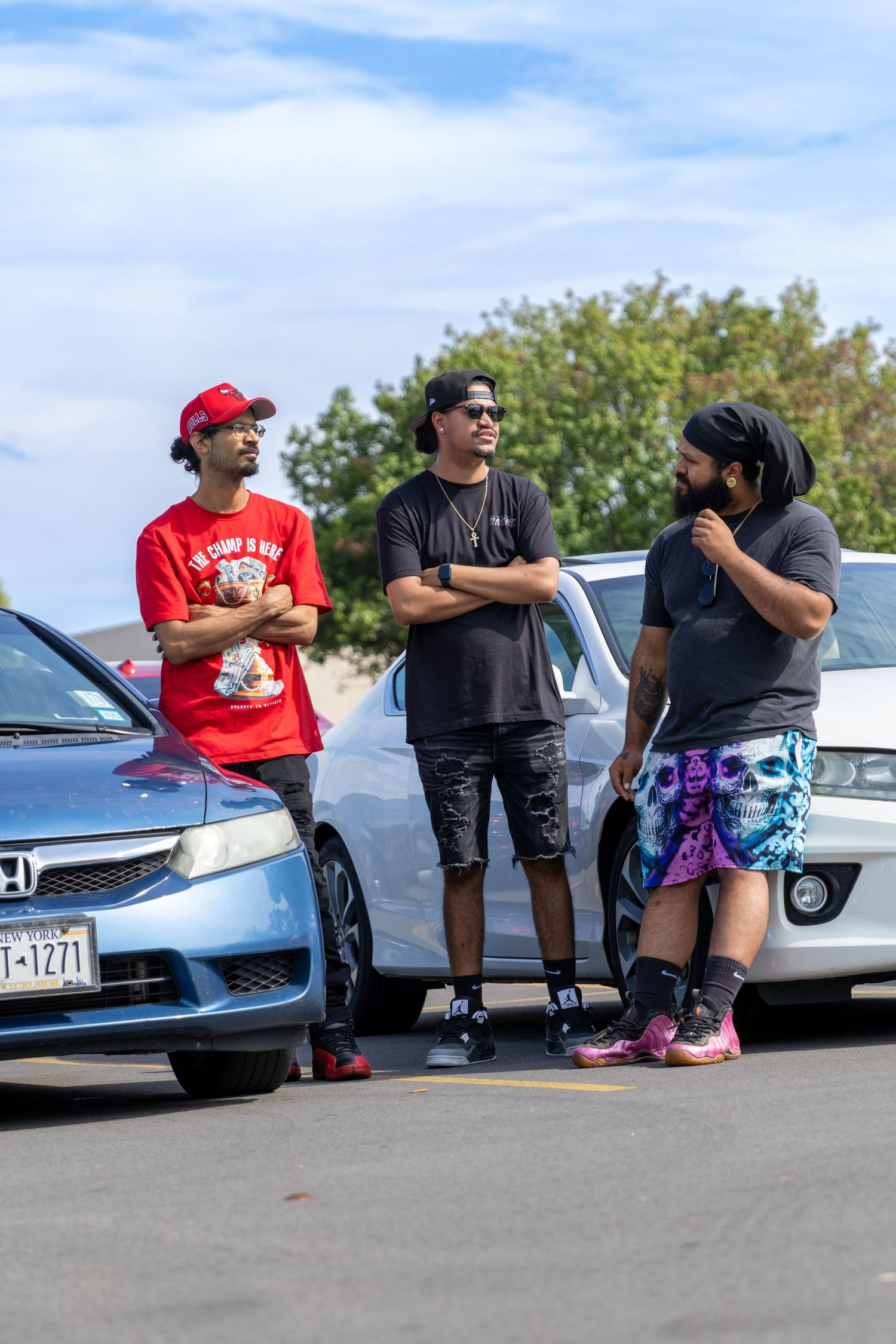 Group of friends relaxing and chatting while sitting on car bumpers in a parking lot.