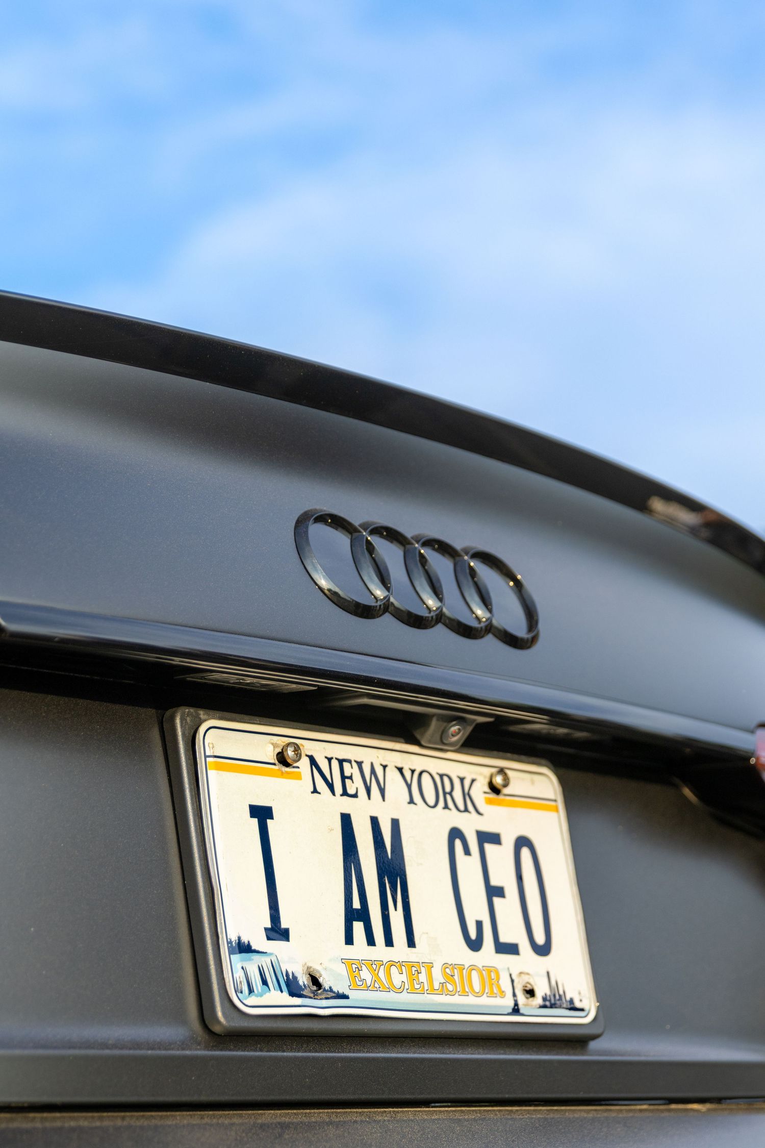 Close-up shots of Audi car trunk showing 'I AM ZEUS' New York license plate against blue sky background.