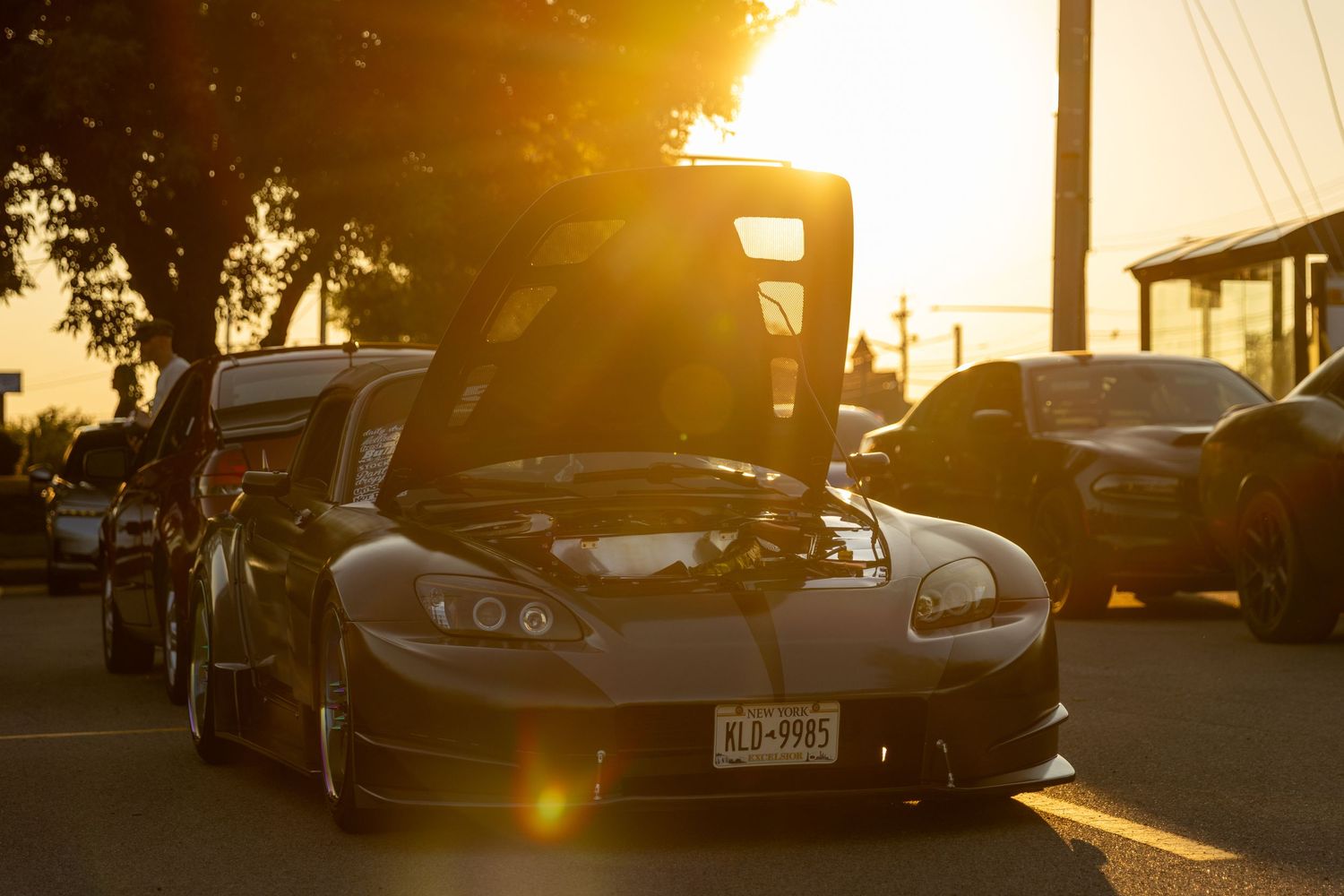 Black Chevrolet Corvette with open hood at sunset with lens flare.