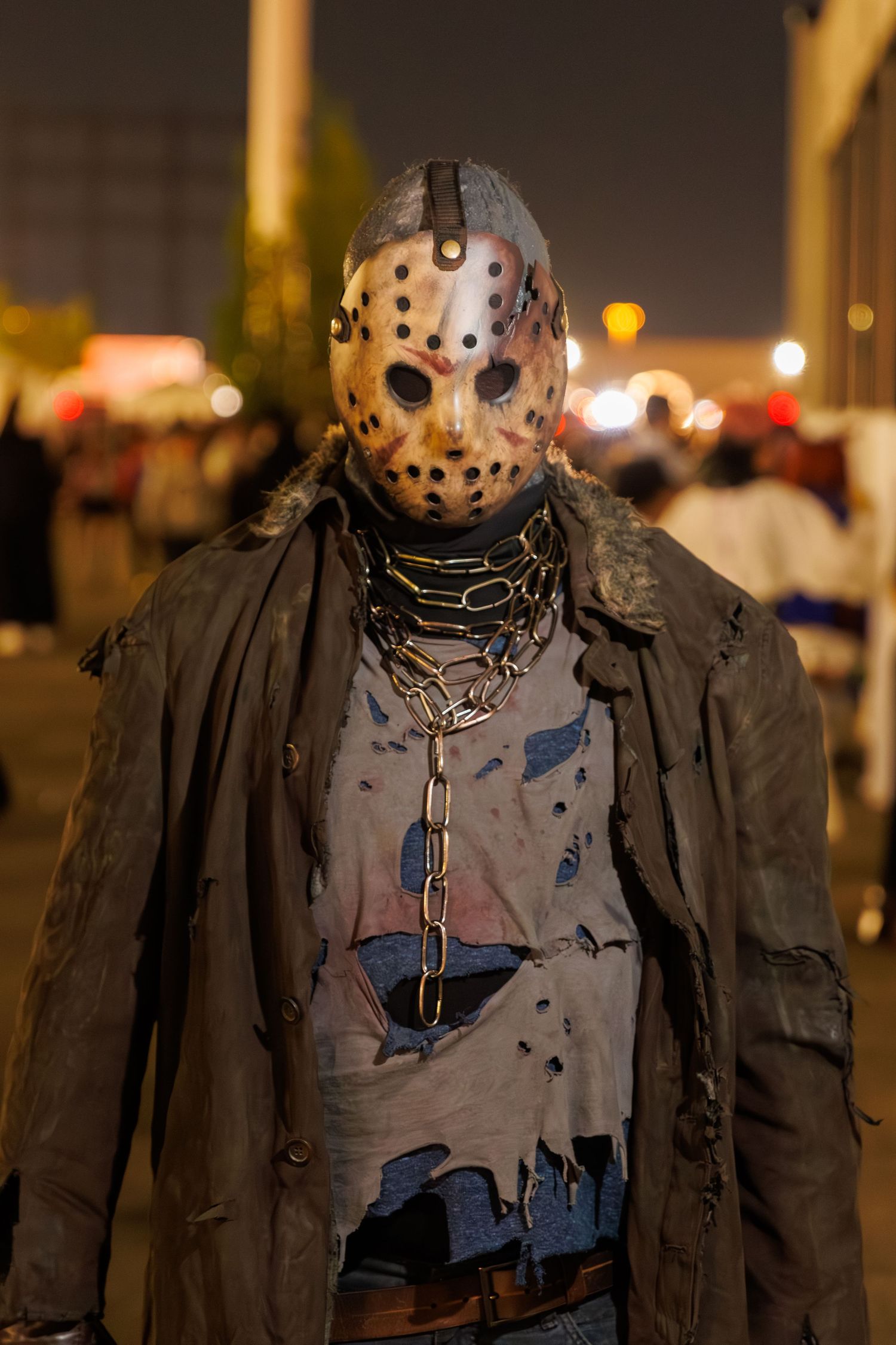 Person dressed as Jason Voorhees in hockey mask, chains, and tattered costume at a Halloween event.