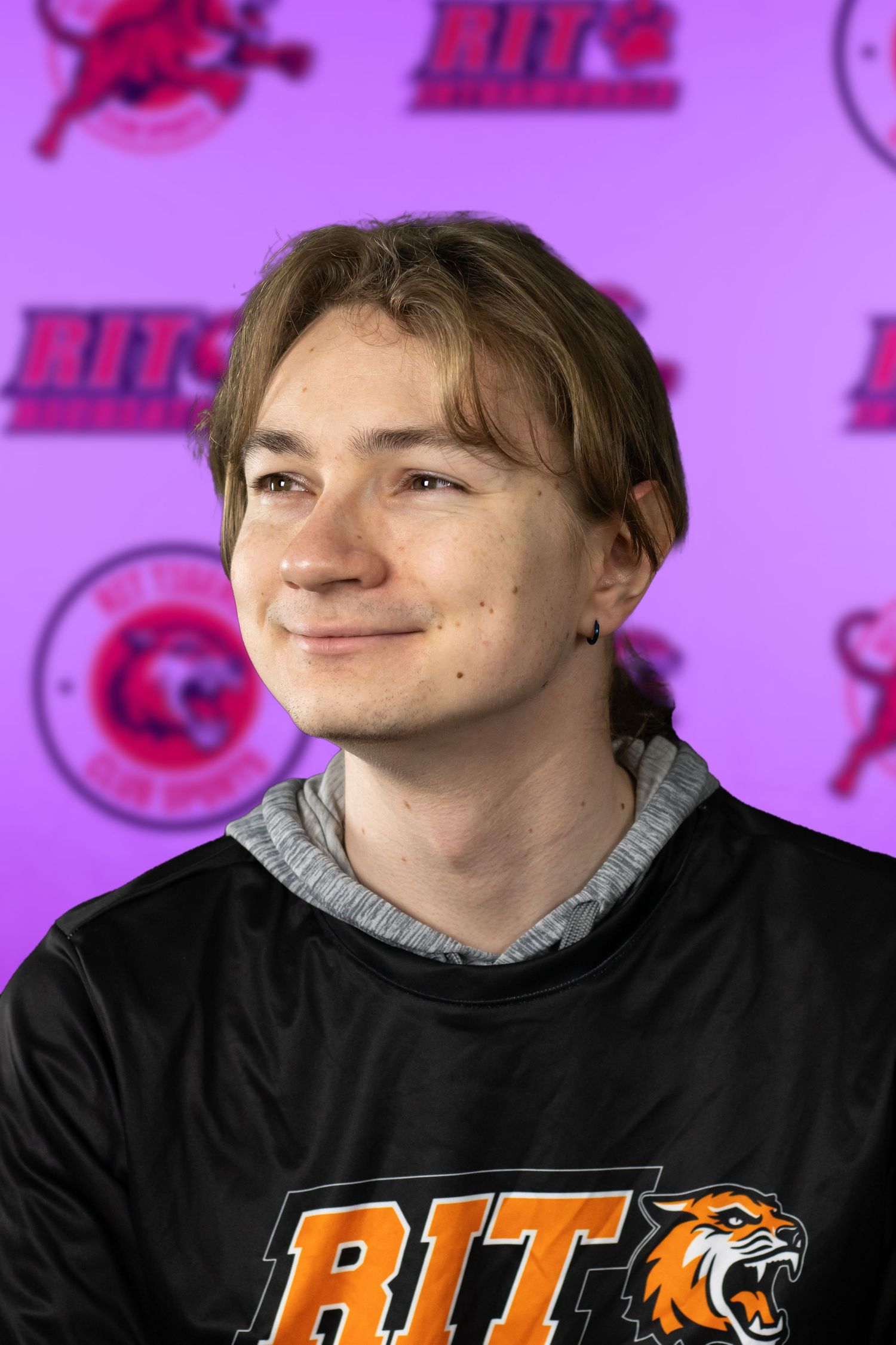 Student athlete poses in front of RIT athletics backdrop wearing black and grey apparel.