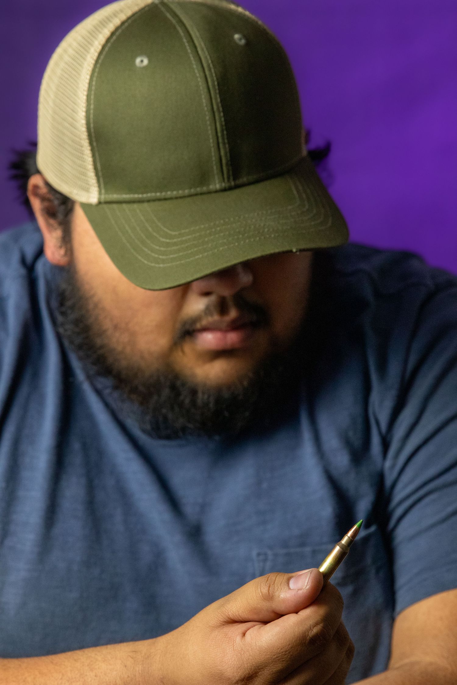 Portrait of someone wearing a green and beige trucker cap against a purple background.