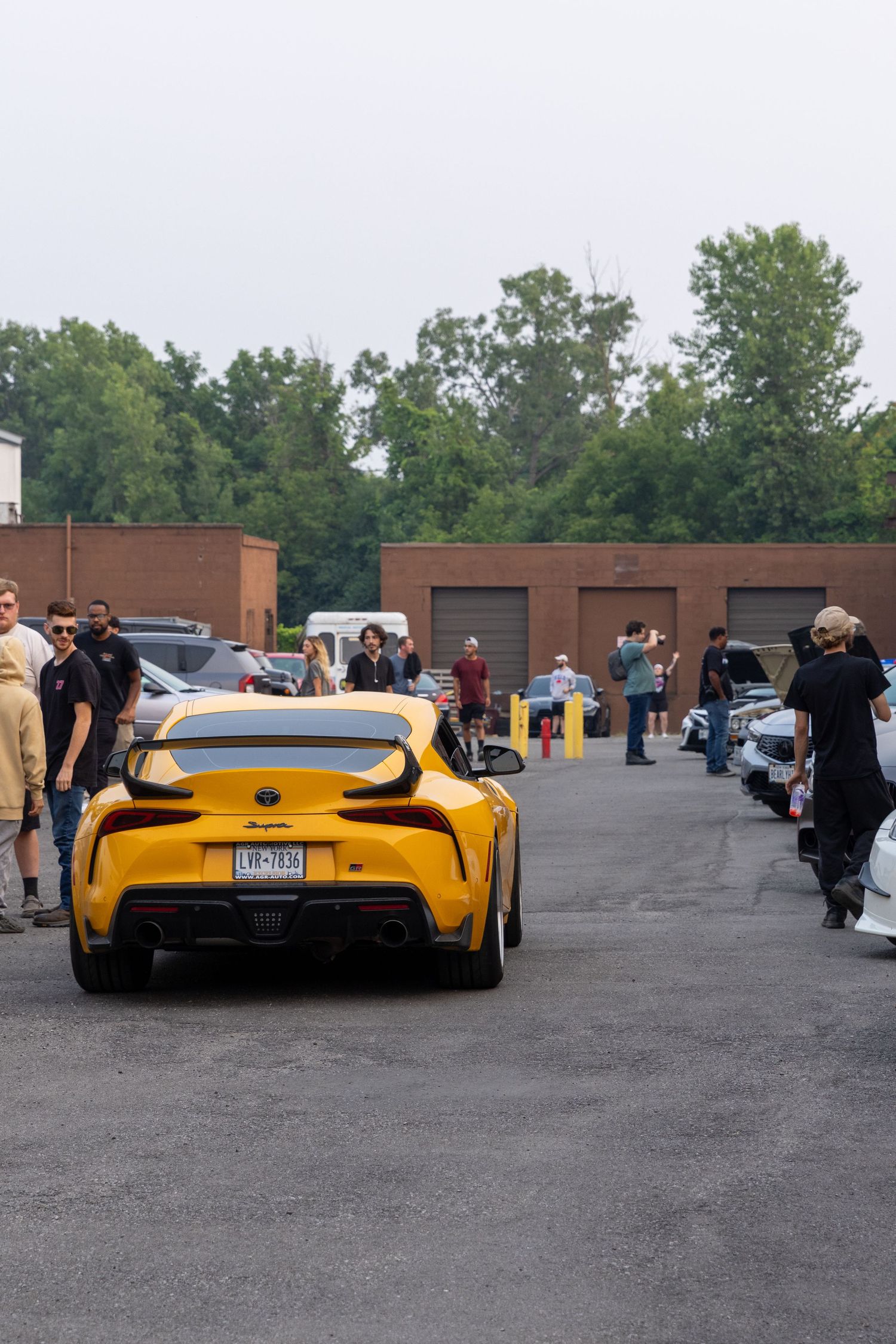A yellow Ferrari sports car parked in a lot with people gathering around to admire it.