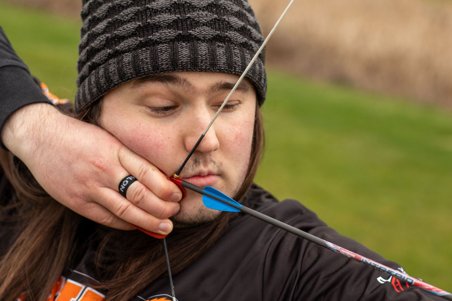 Close-up of archer drawing bow string while wearing knit cap during practice.