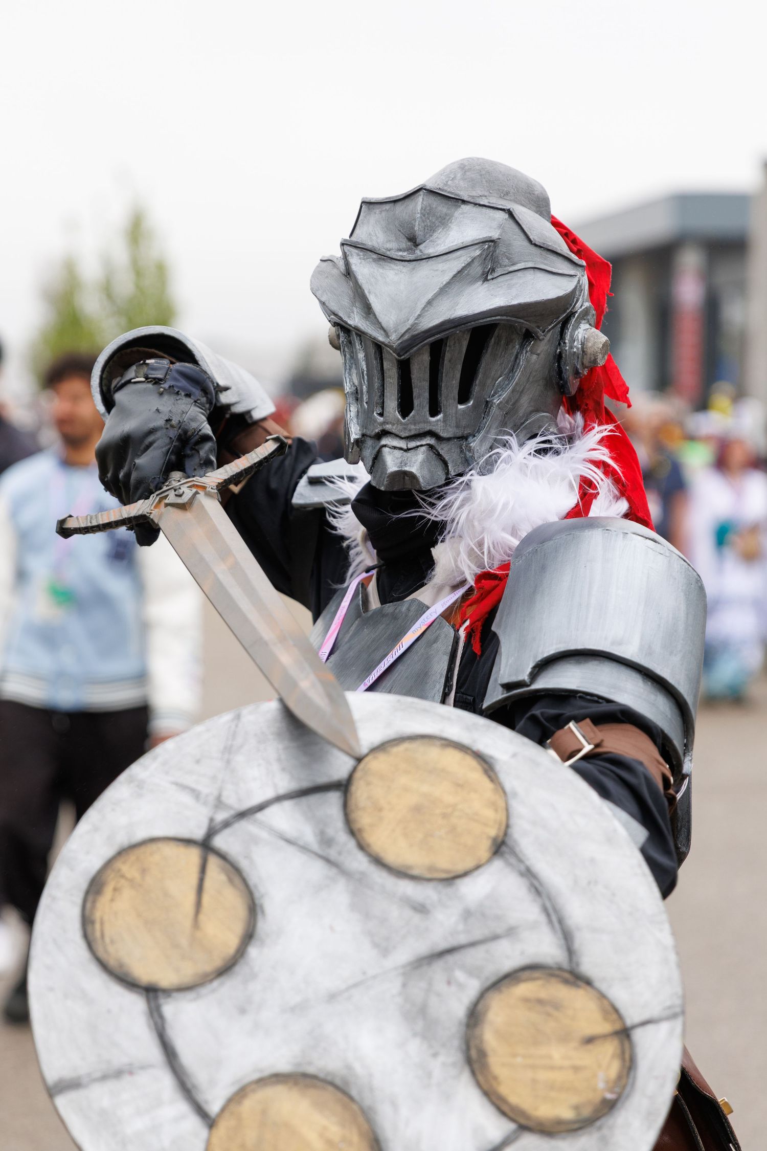 Cosplayer in full silver knight armor wielding a sword and shield at a convention.