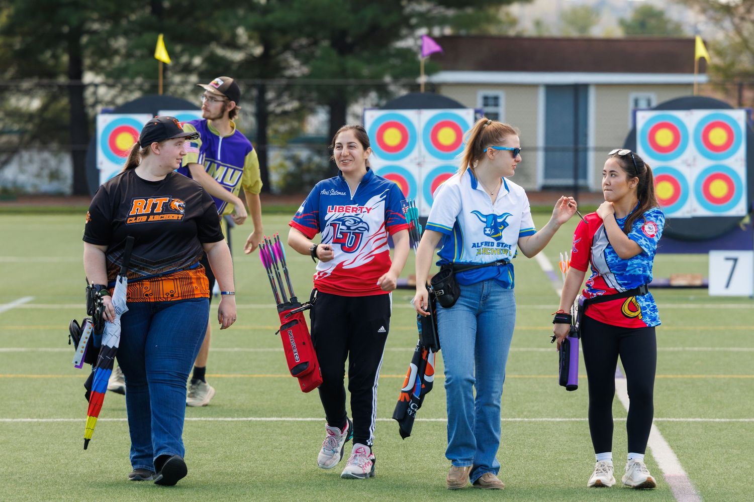 Female archers walking across a field at an outdoor archery tournament.
