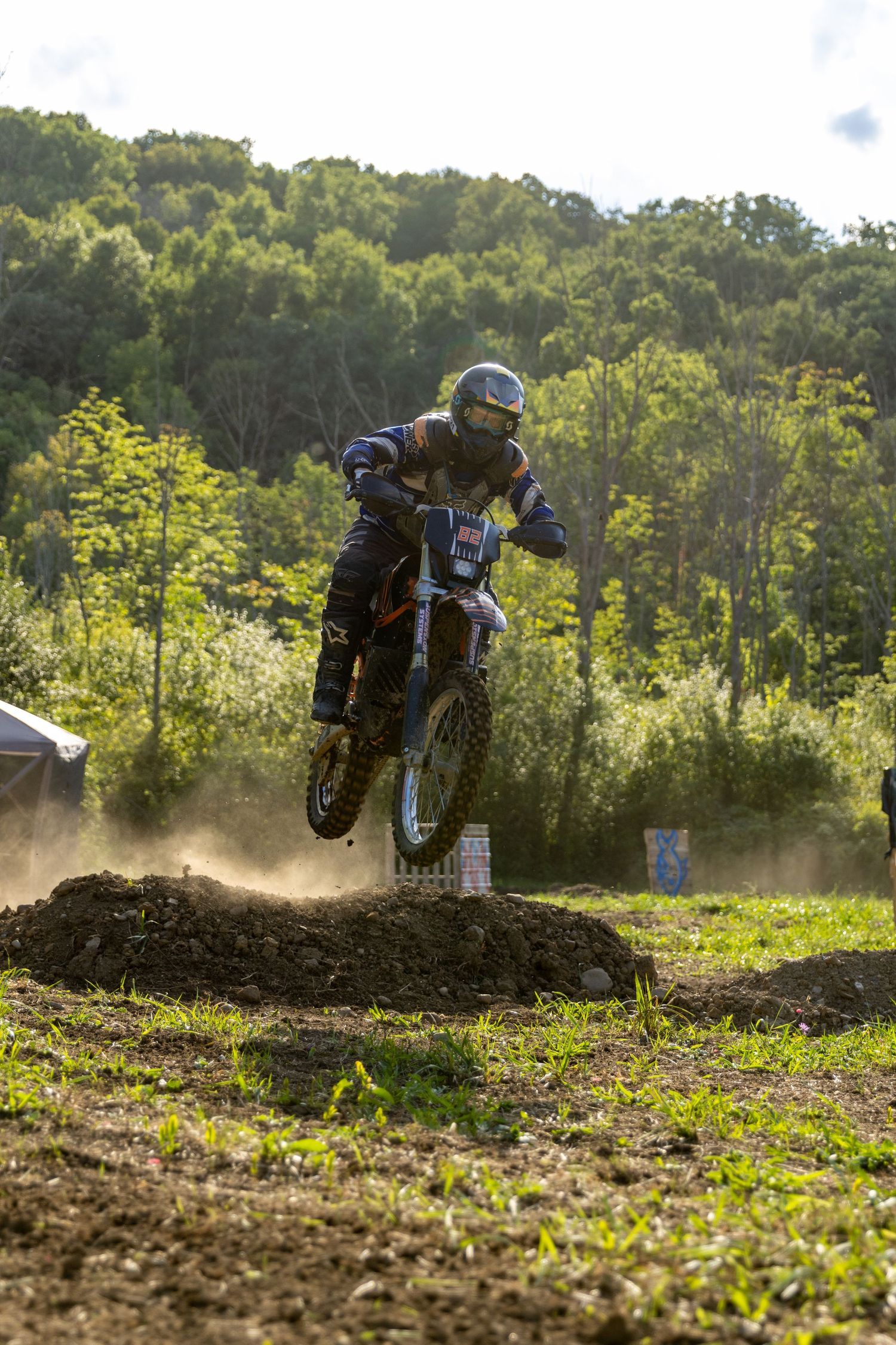 Motocross rider launches over dirt jump during intense off-road racing sequence on wooded course.