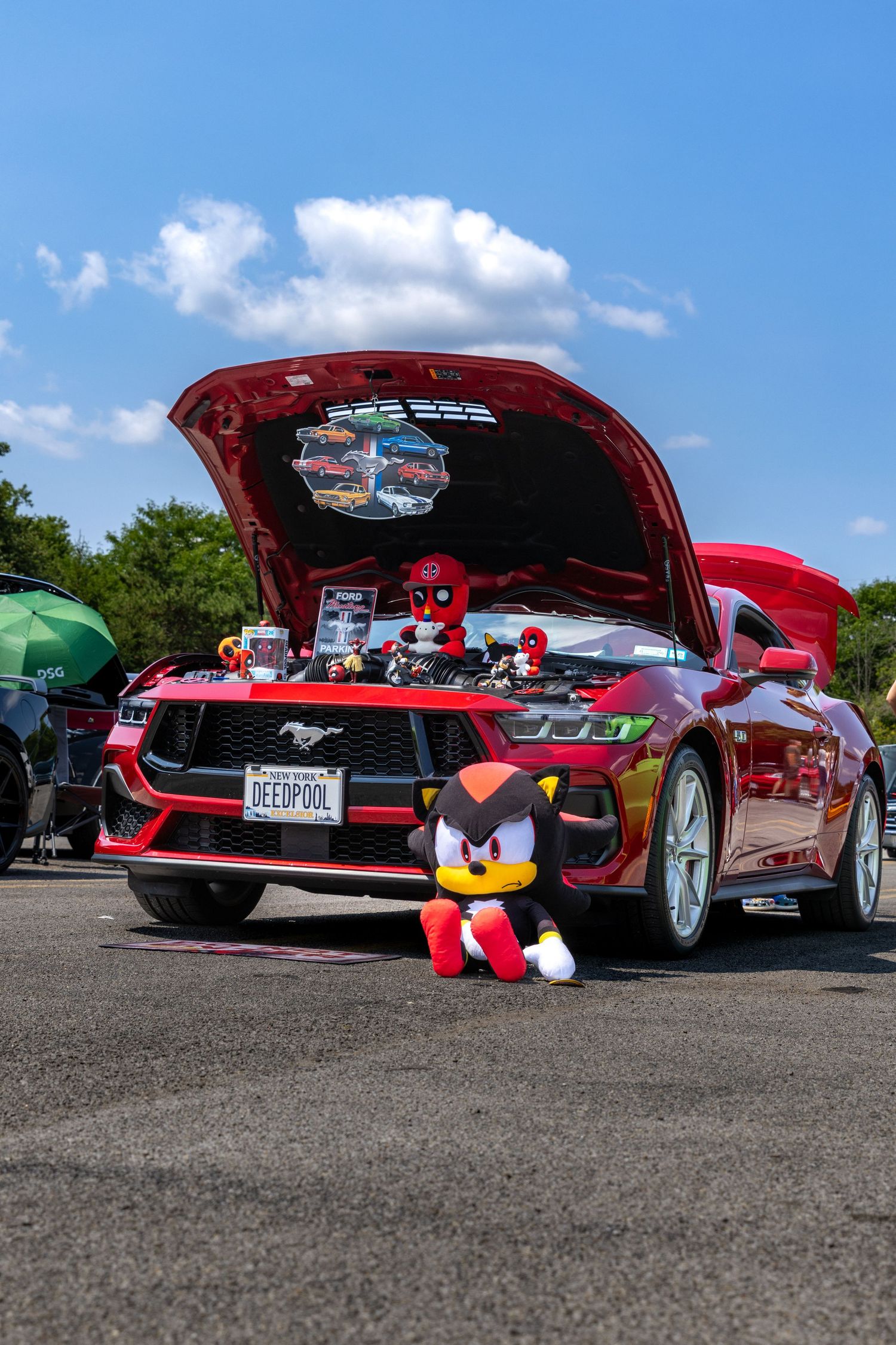 Low-angle shot of a red vintage Ford Mustang with its hood up at a classic car show on a sunny day.