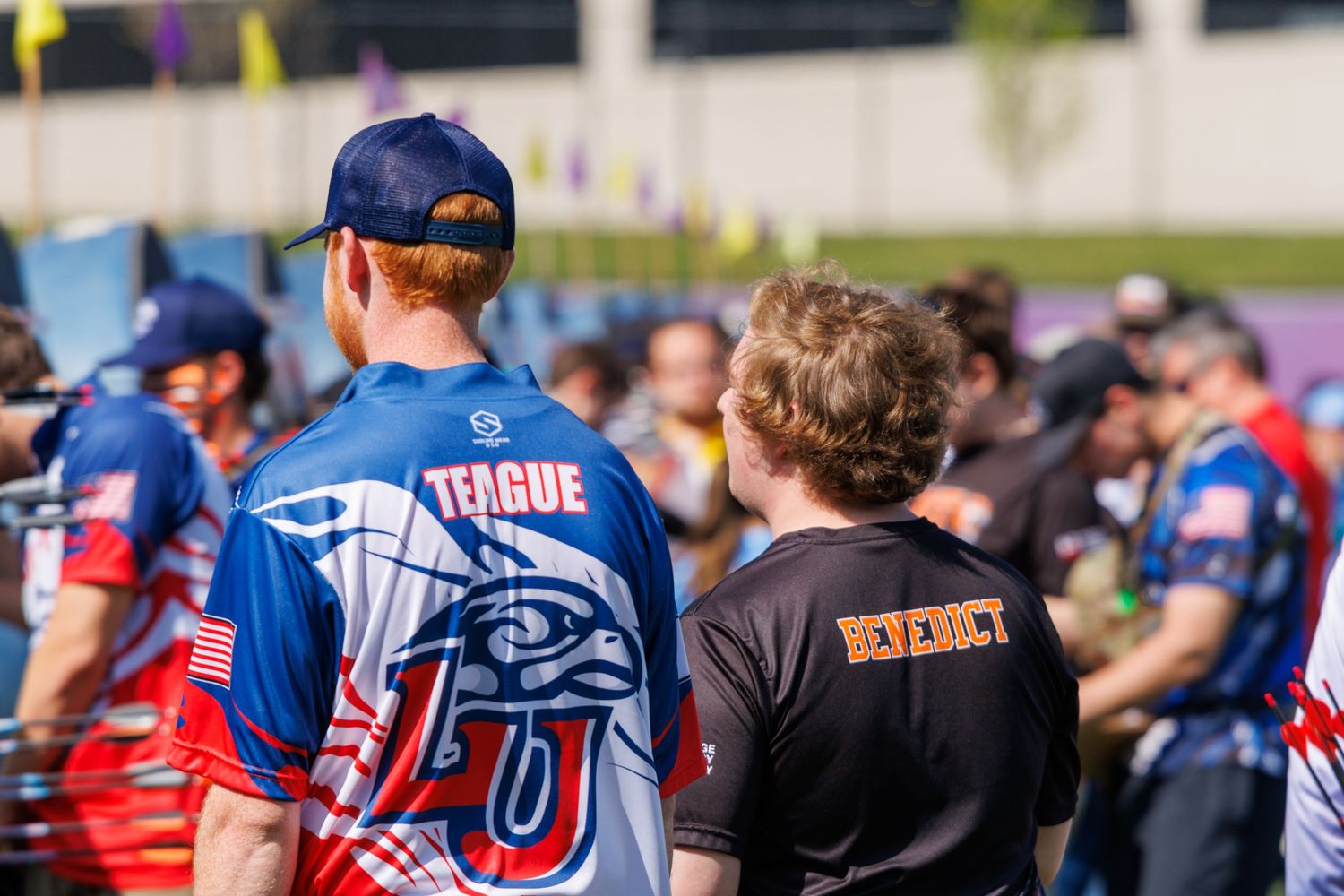Two archers wearing Teague and Benedict team jerseys stand together at an outdoor archery tournament.