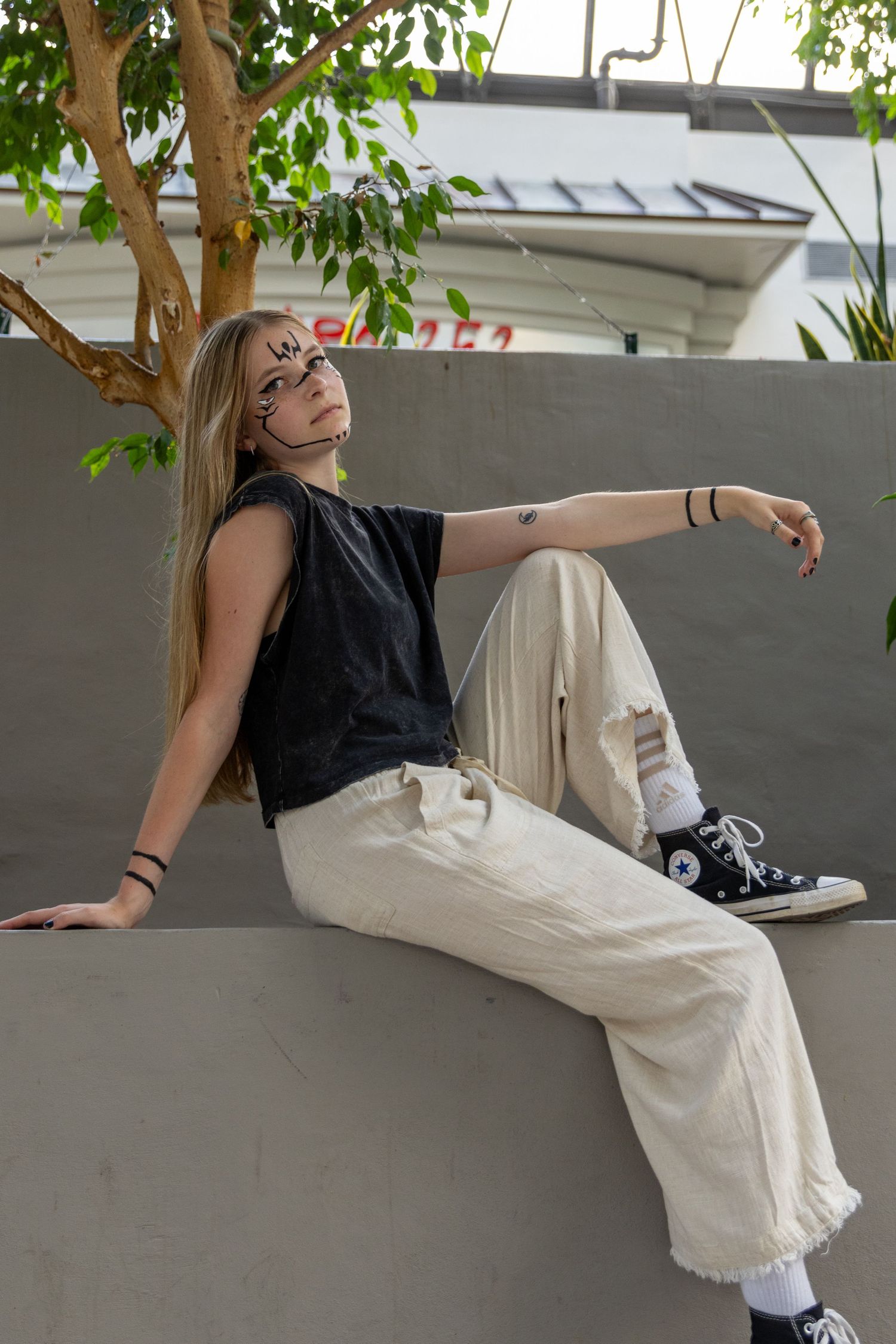 Person wearing a black top and white pants sits casually against a wall with black sneakers.