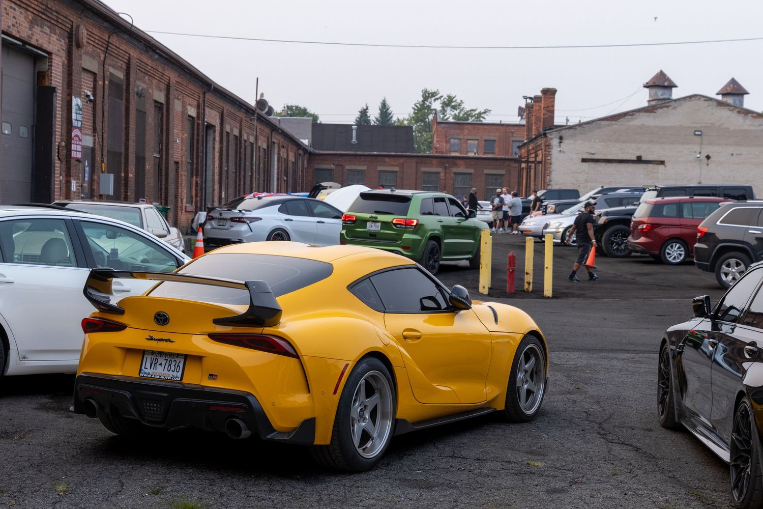A bright yellow sports car photographed in a parking lot next to other vehicles on an overcast day.