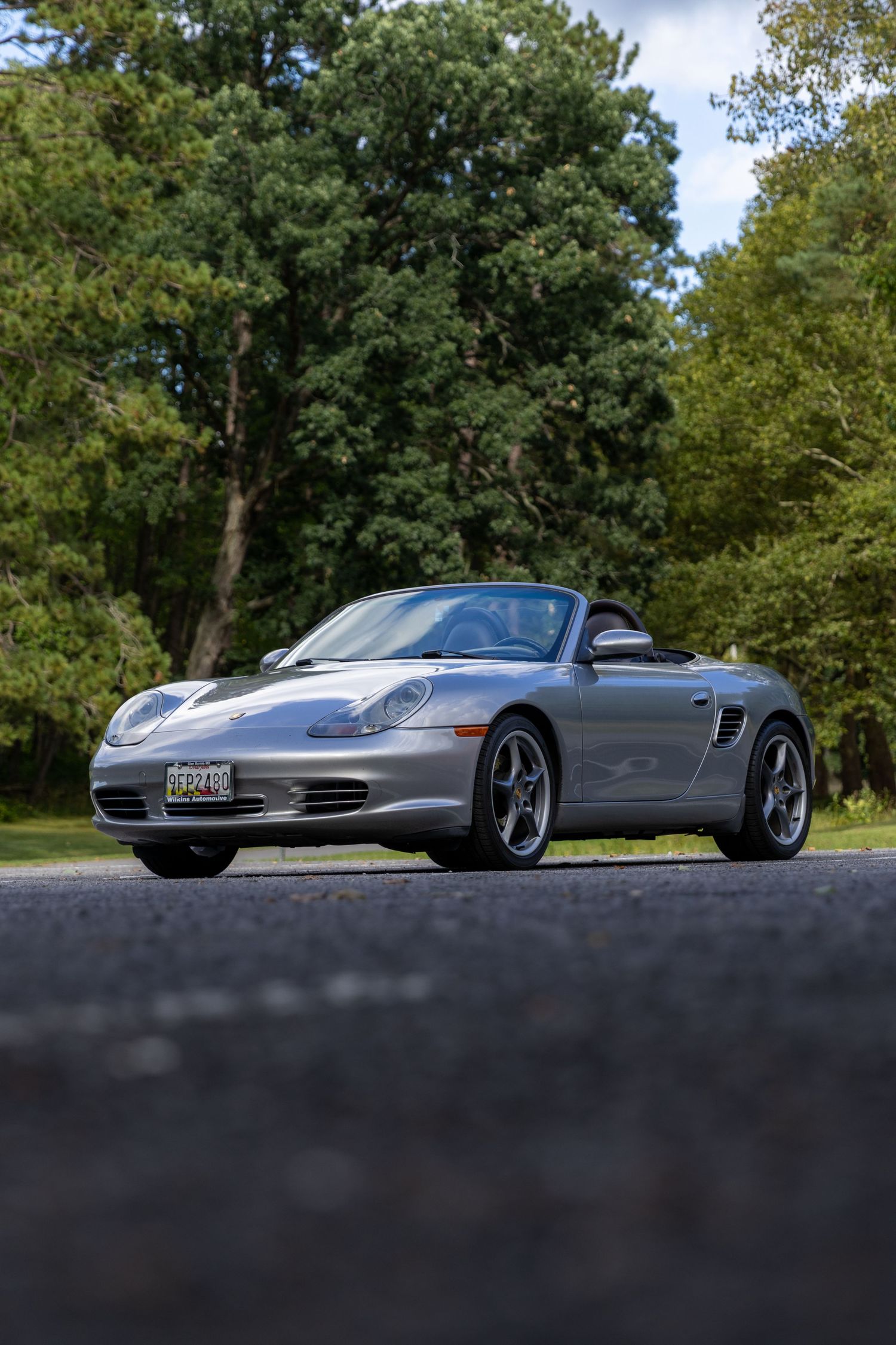 Low-angle view of silver Porsche 911 Turbo parked on asphalt against green trees in natural setting.