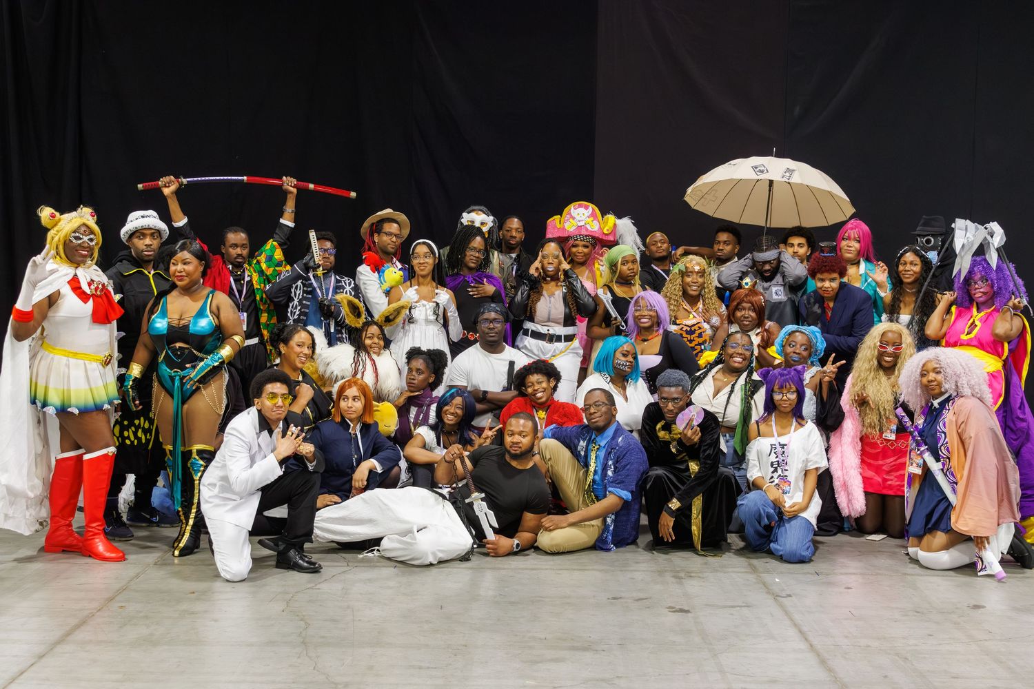 Large group of diverse cosplayers posing together at a convention, wearing colorful anime and fantasy costumes.