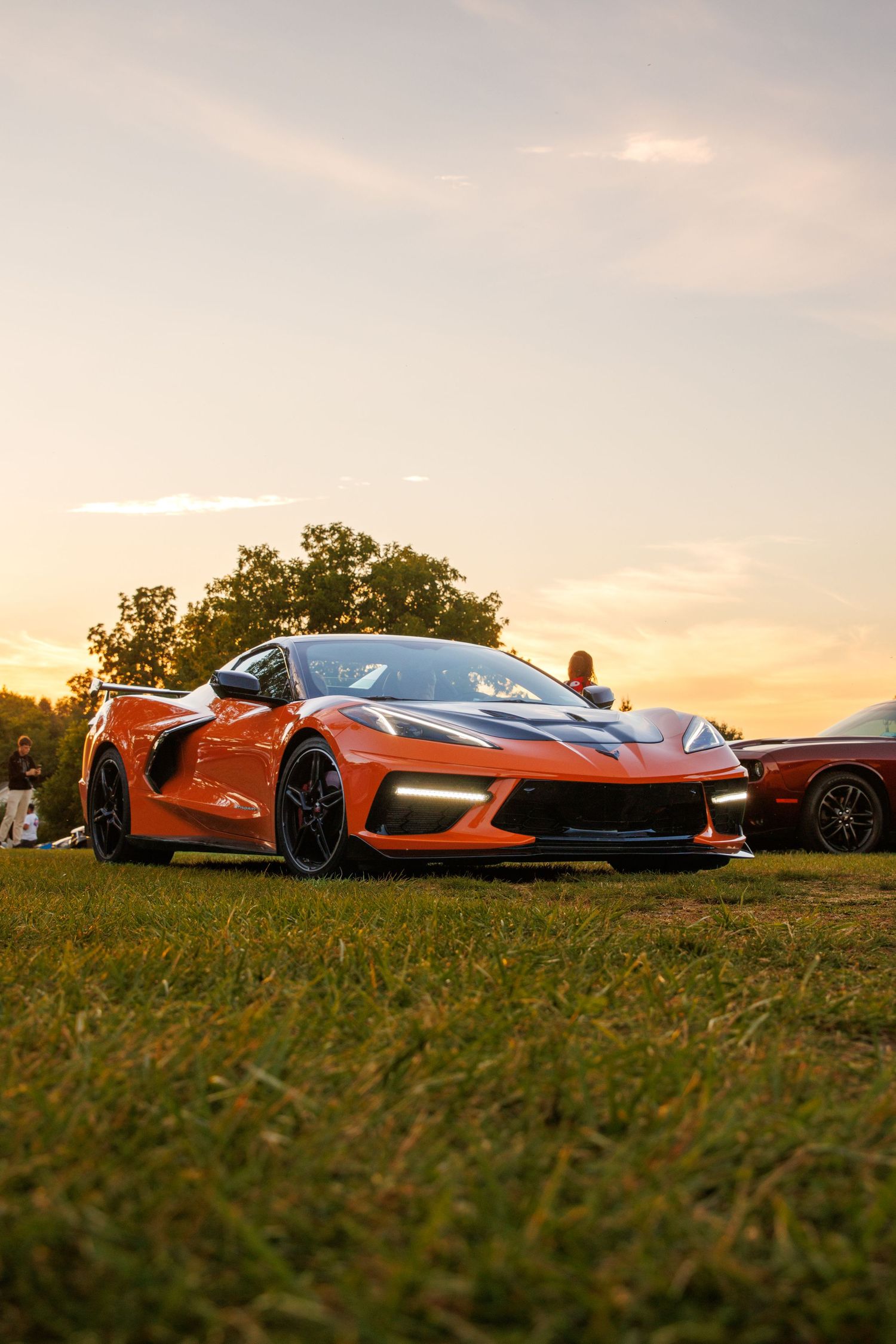 Three orange supercars parked on grassy field during golden sunset with dramatic lighting.