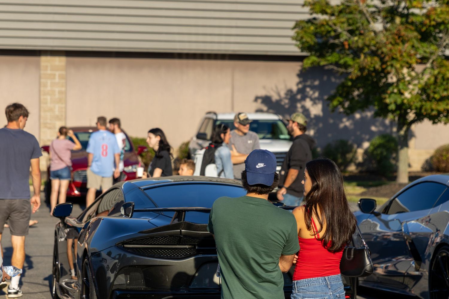 People gathered in a parking lot near parked cars during what appears to be a community or social event.