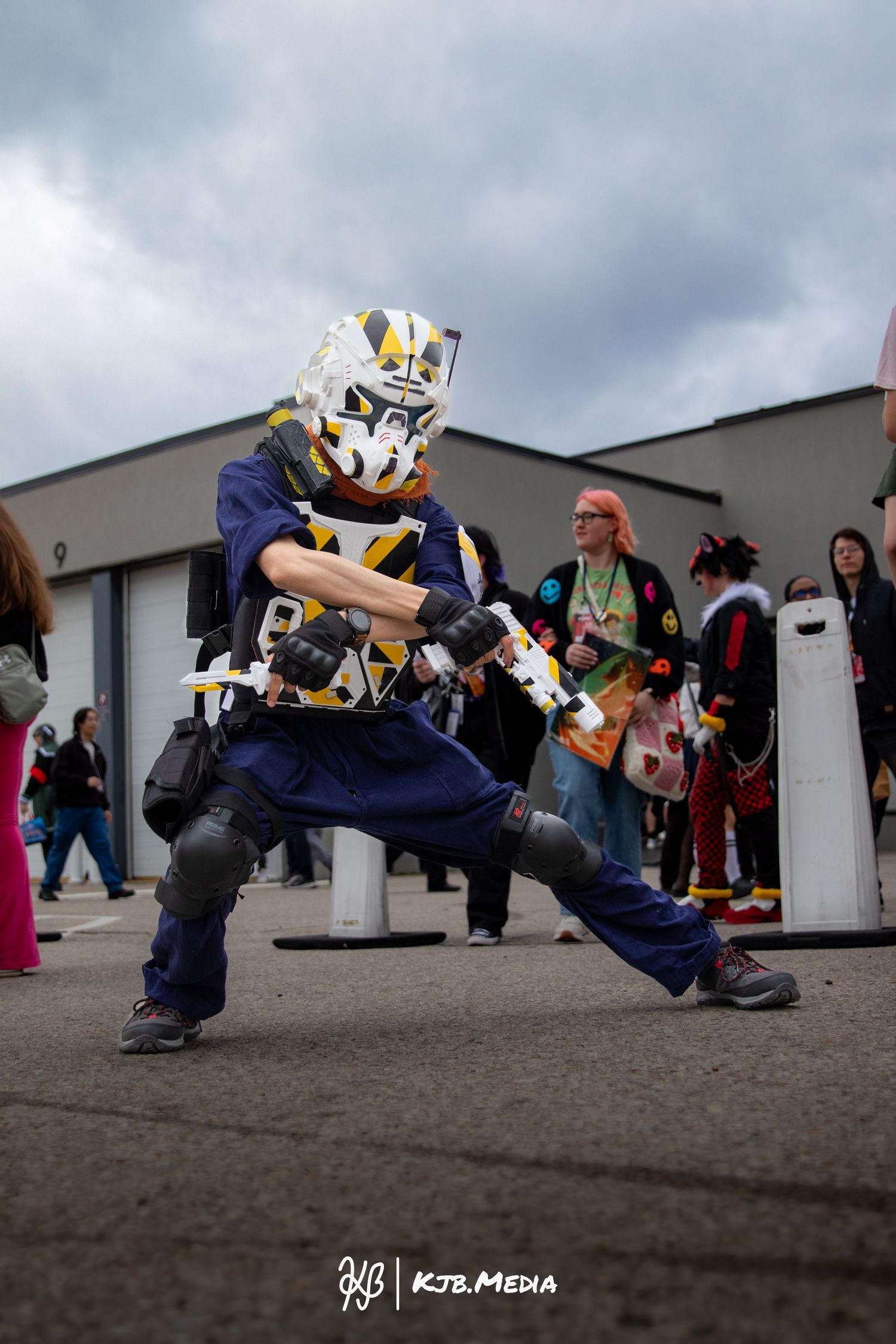 Cosplayer in robot-inspired mask and navy uniform strikes action pose at convention.