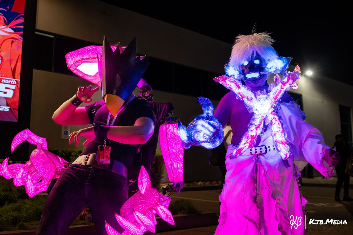 Glowing neon cosplay characters illuminated in pink and purple lighting at night.