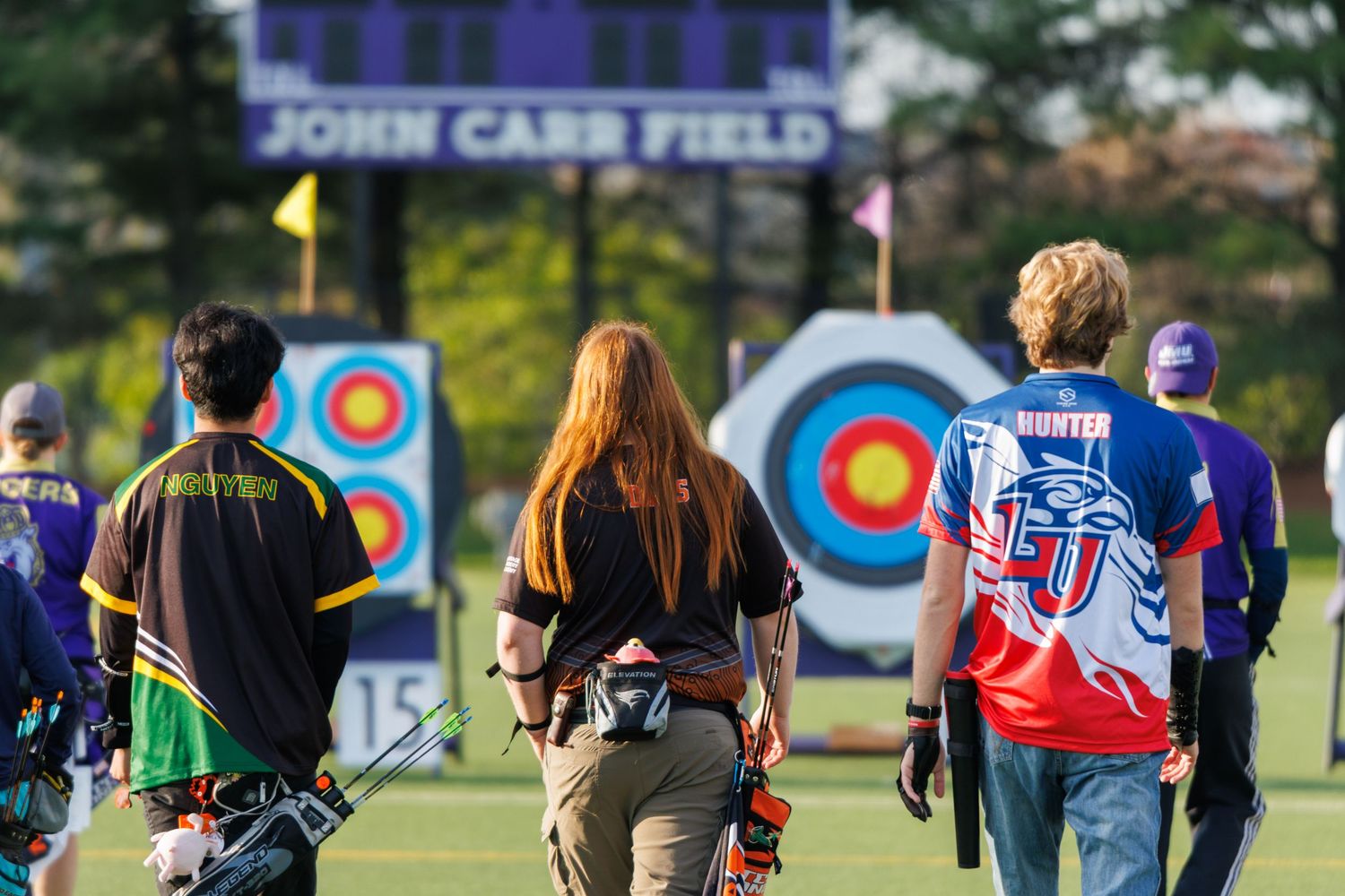 Archers walk toward colorful targets at John Carr Field during outdoor archery tournament.