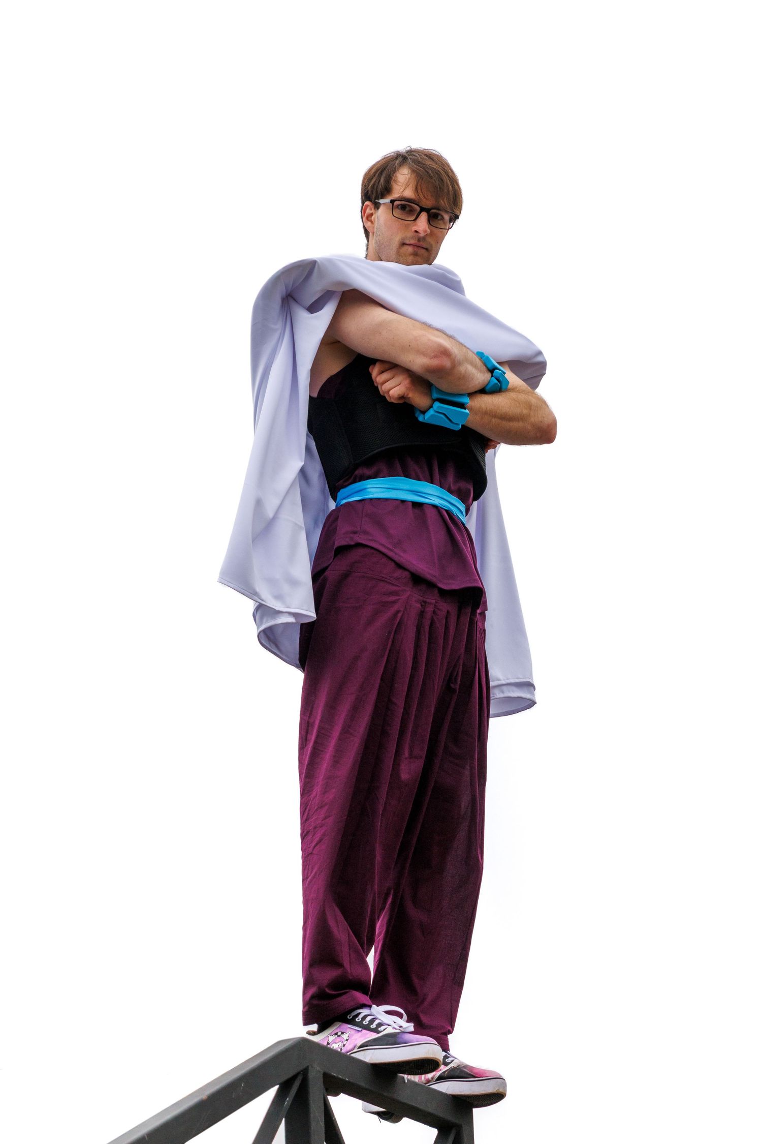 Man in purple pants, black top, and white cape stands confidently with arms crossed on elevated platform.