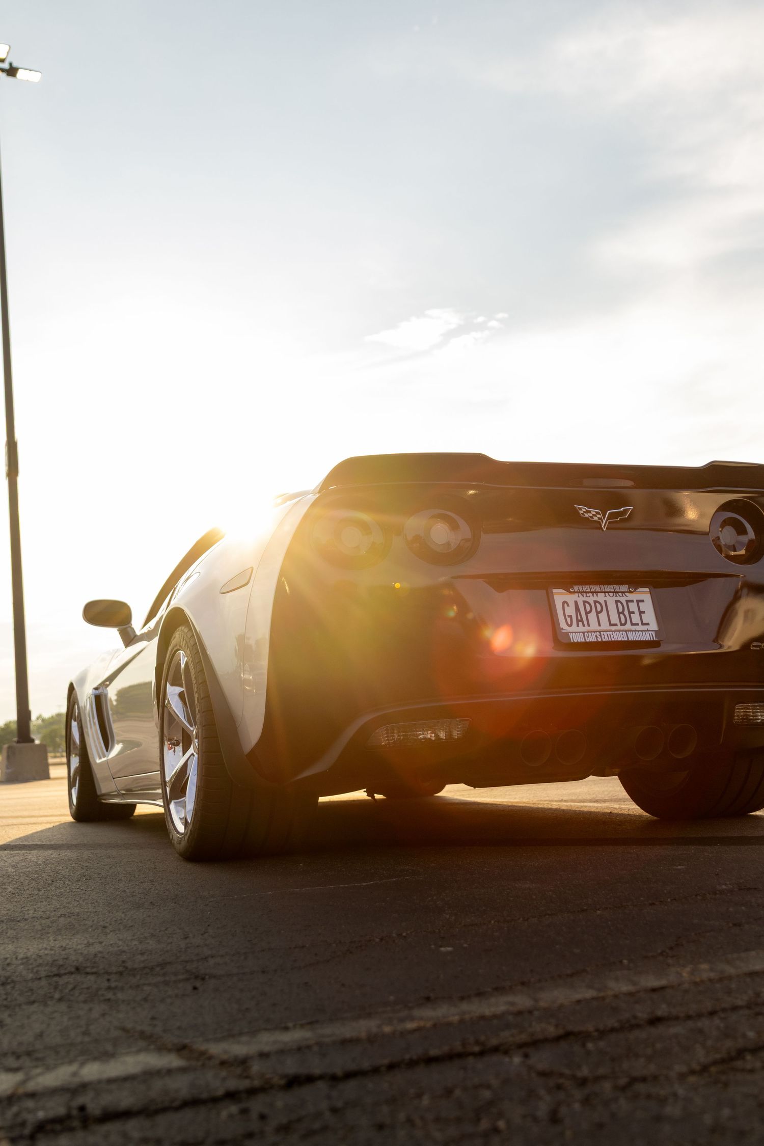 Black sports car rear view silhouetted against dramatic sunset with sun flare creating atmospheric lighting effect.
