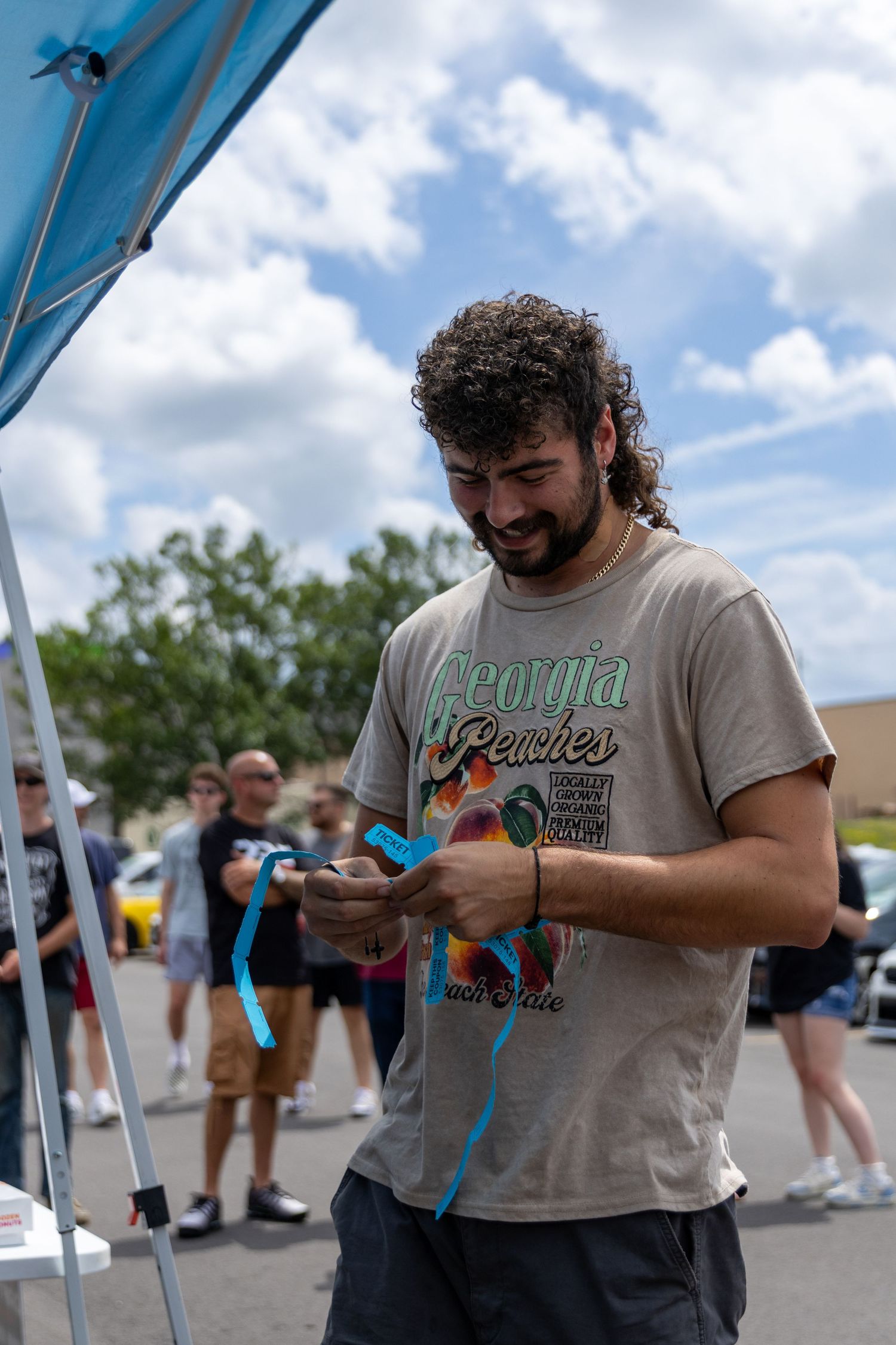 A man with a beard stands outdoors checking his phone during a sunny day while smiling.