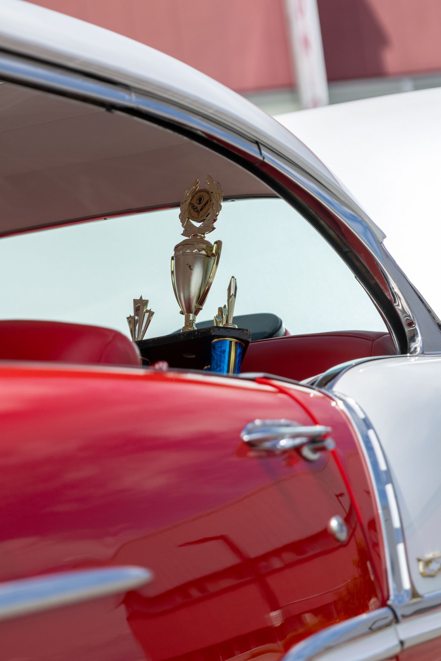 Chrome trim and red paint details of a vintage car's roofline against a bright sky.
