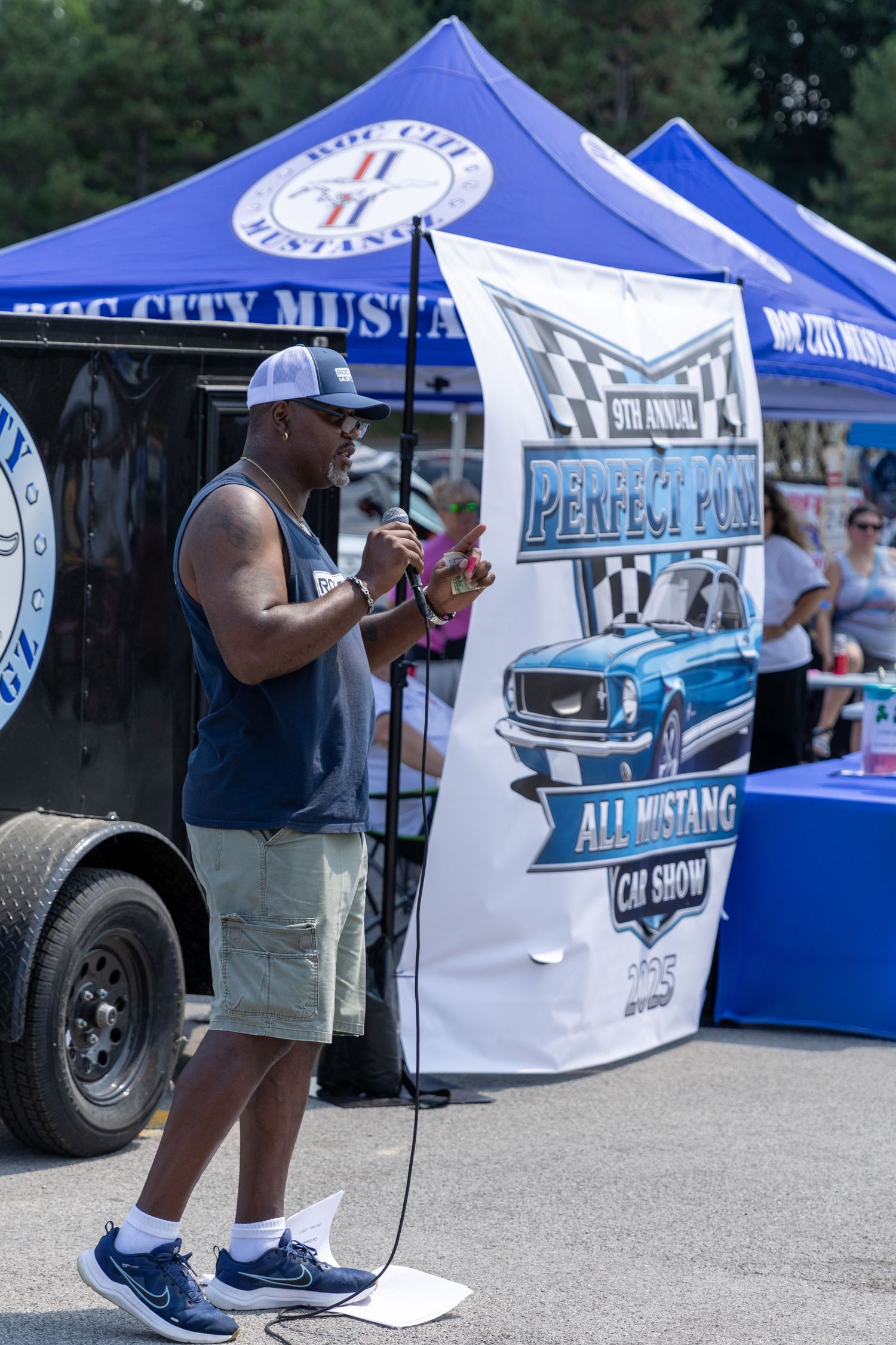 Outdoor car show vendors with white and blue tents displaying automotive merchandise and signage.
