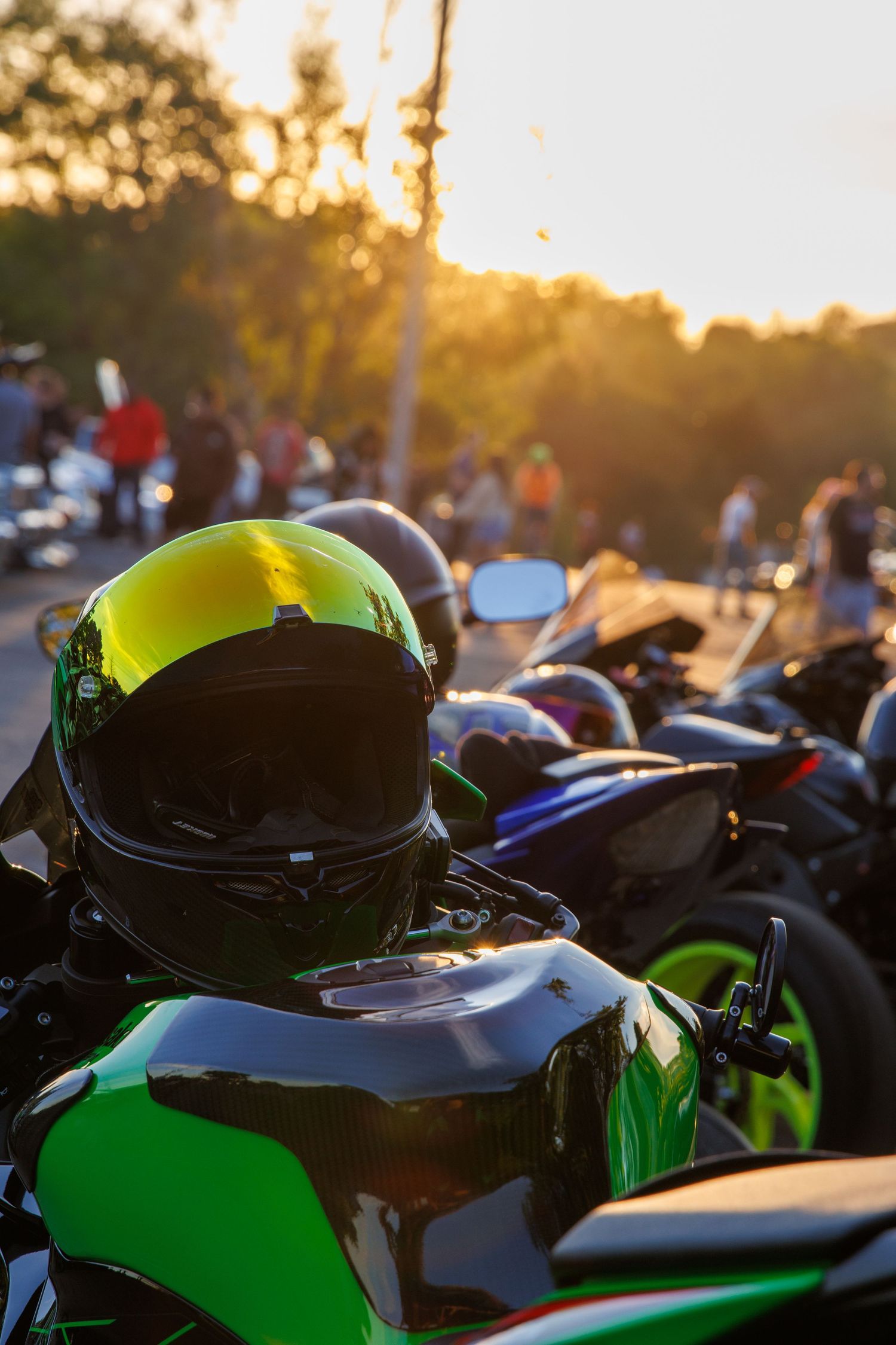 A motorcycle with a neon green helmet sits parked at a sunset bike meetup with other motorcycles in the background.