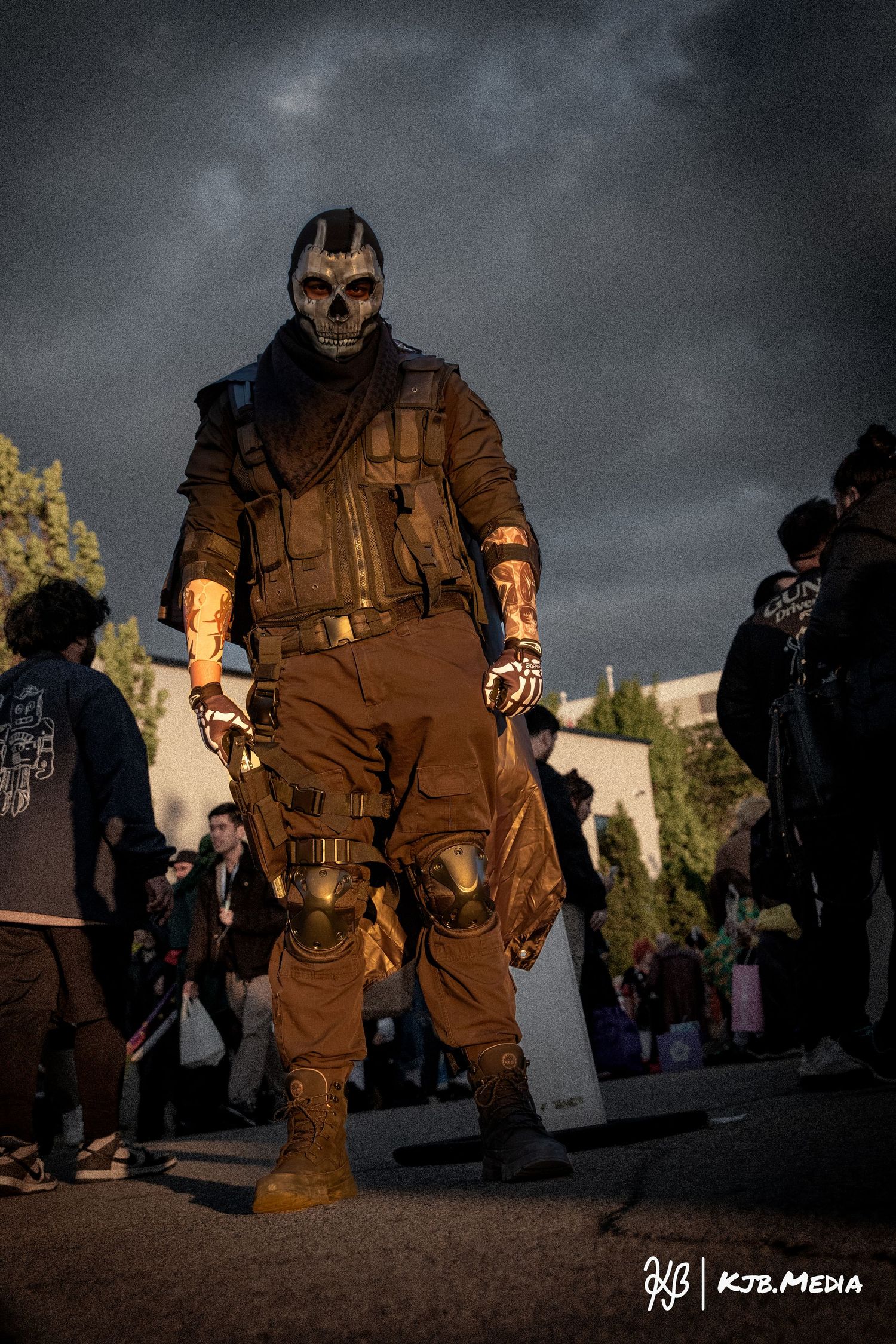 Imposing figure in tactical gear and skull mask stands menacingly against stormy sky at cosplay event.