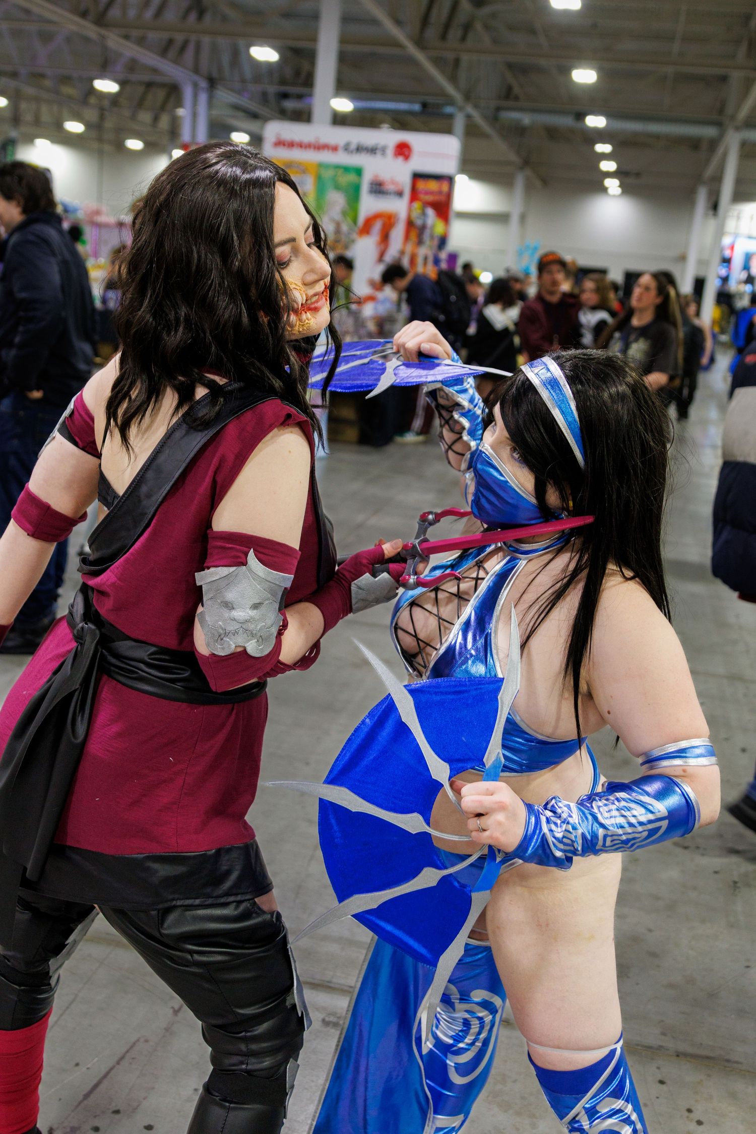 Two cosplayers dressed as Mortal Kombat characters Mileena and Kitana pose fighting at a comic con.