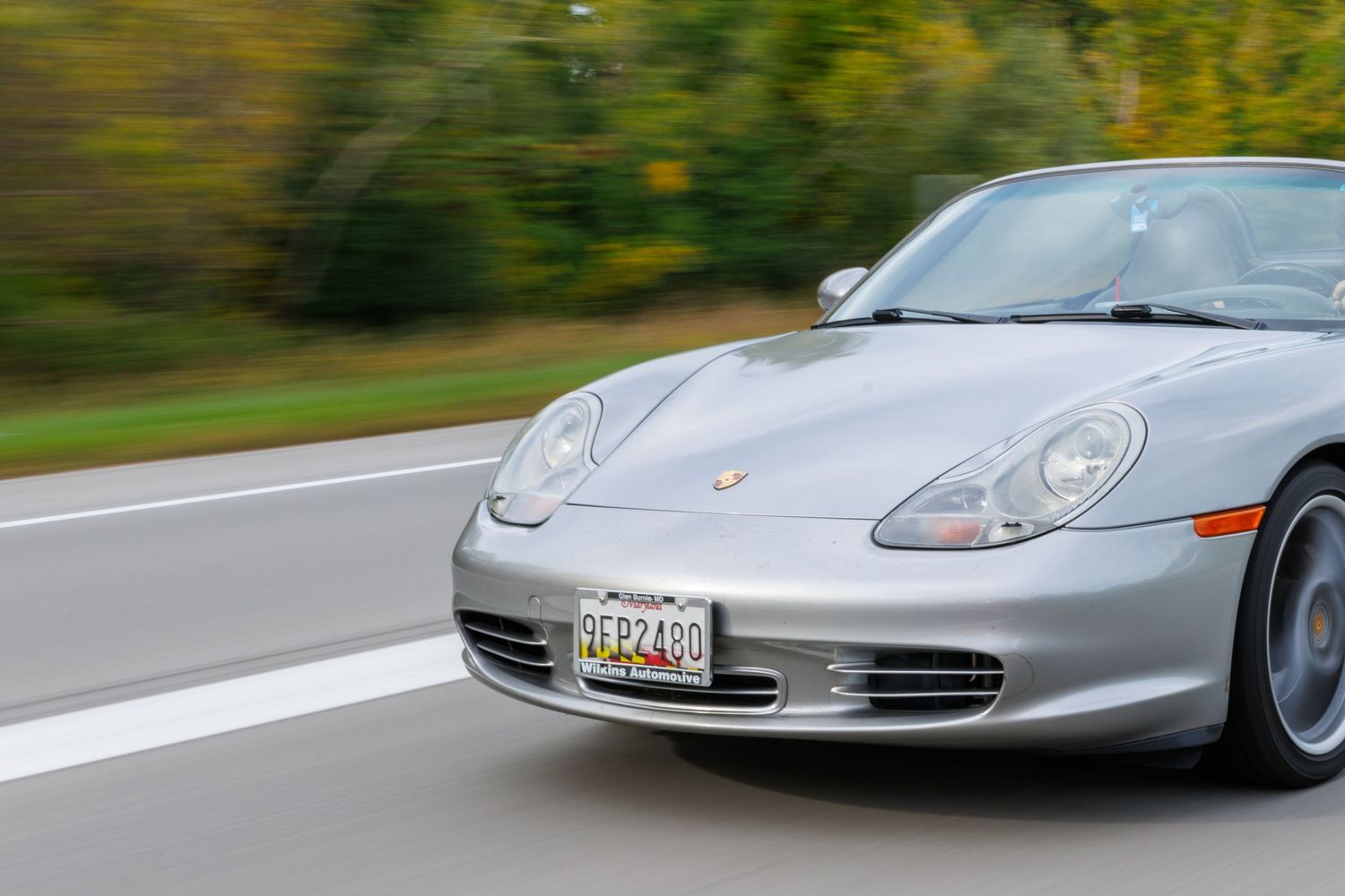 A lineup of silver Porsche sports cars parked on a road with autumn foliage in the background.