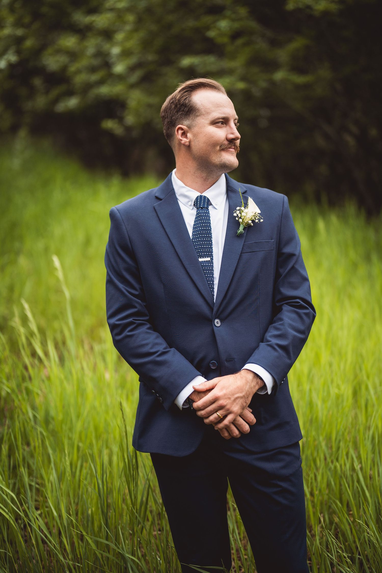 Creative portrait series of a groom in a navy blue suit posing in a grassy field.