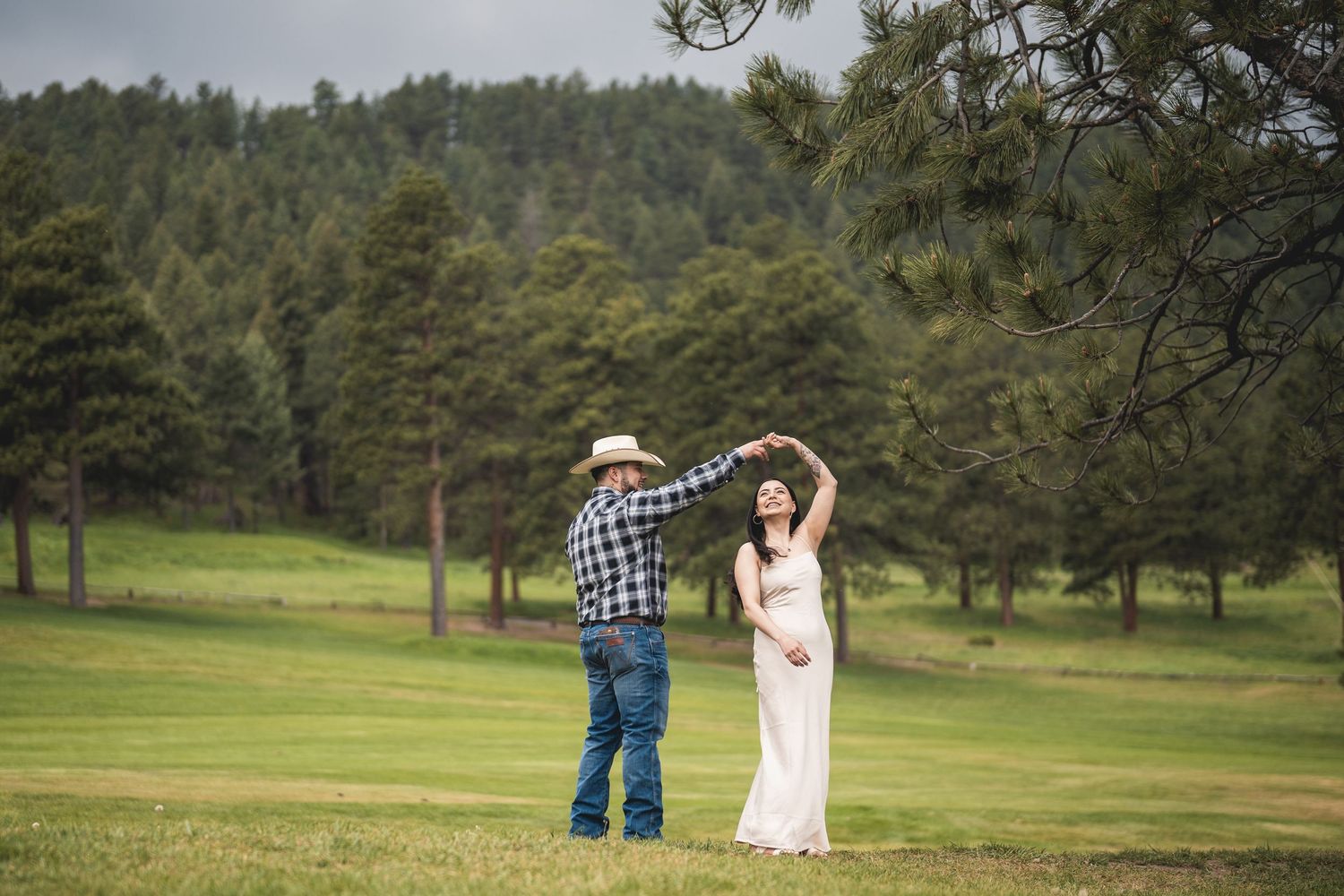 Couple dancing together in a scenic mountain meadow with pine trees in the background.