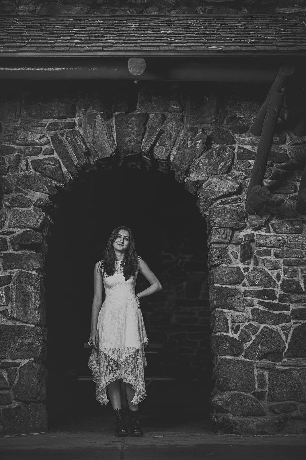 Dramatic black and white portrait against stone archways and textured brick wall.