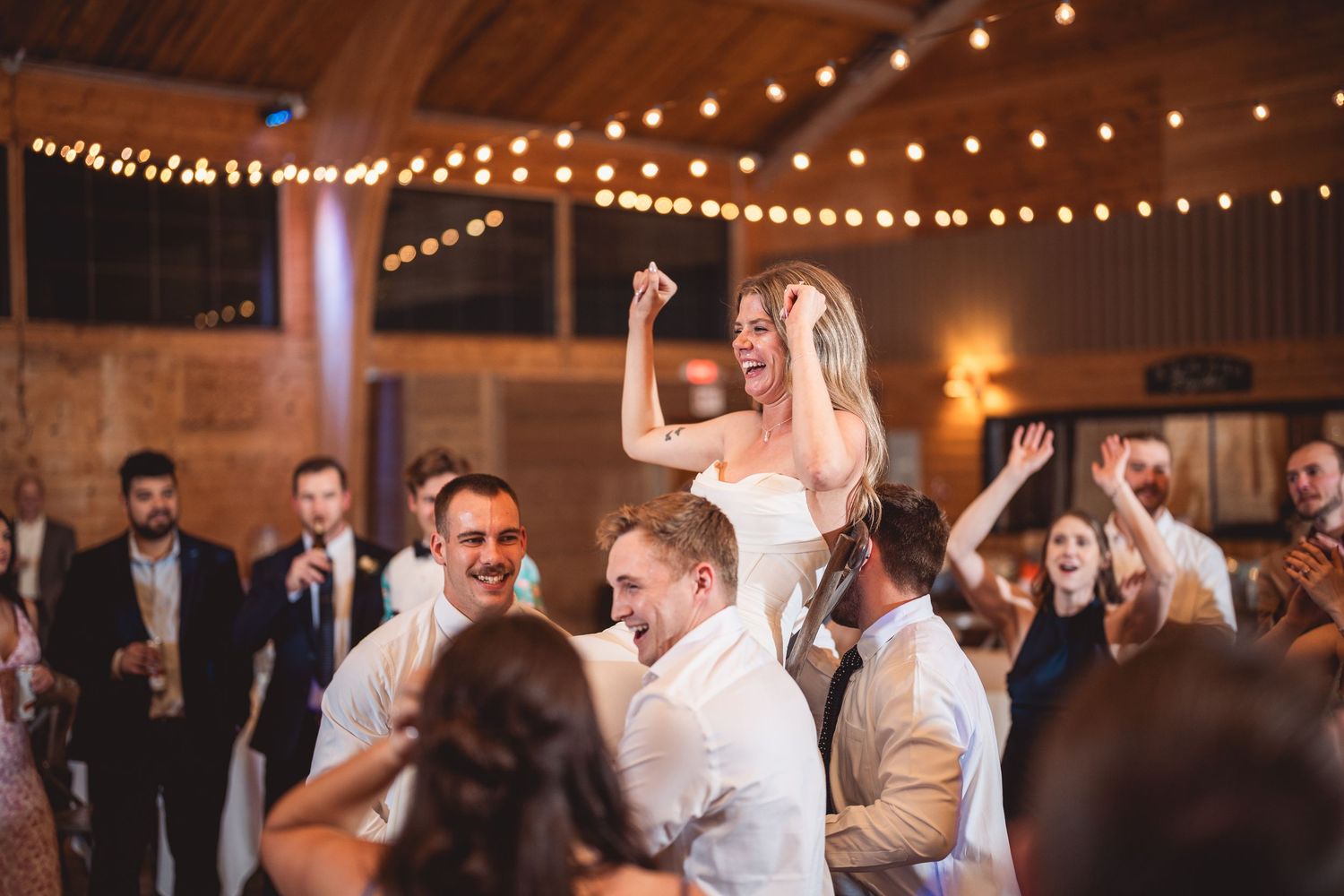 Guests enjoying a festive dance celebration at indoor wedding reception with string lighting.