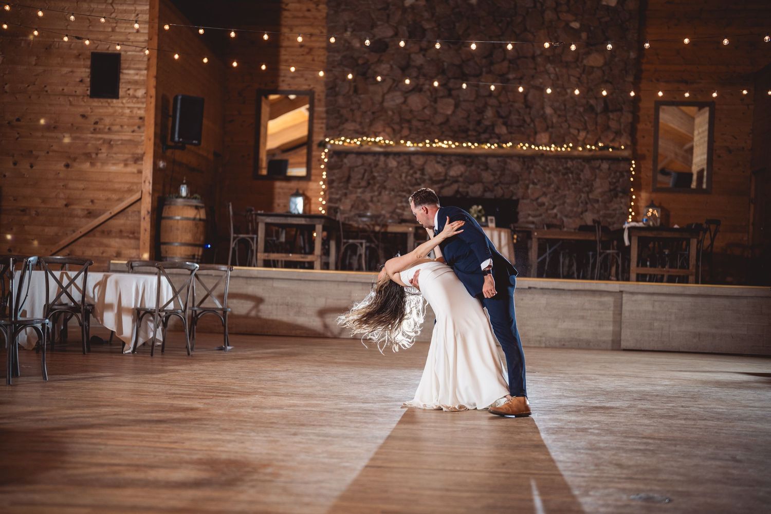 String lights illuminate a rustic barn dance floor where a couple shares their first dance.