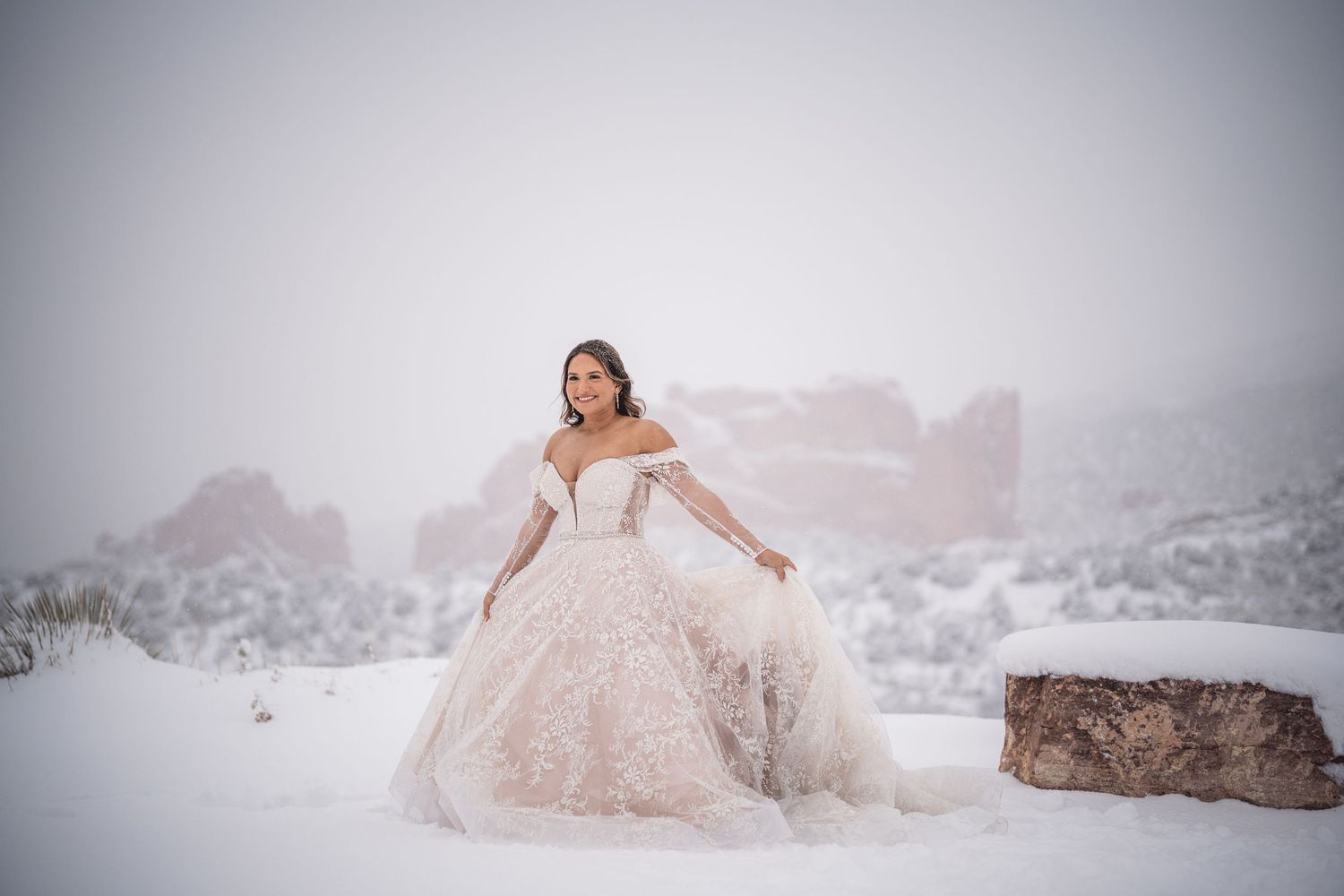 Person in flowing white dress poses dramatically in snowy winter landscape.