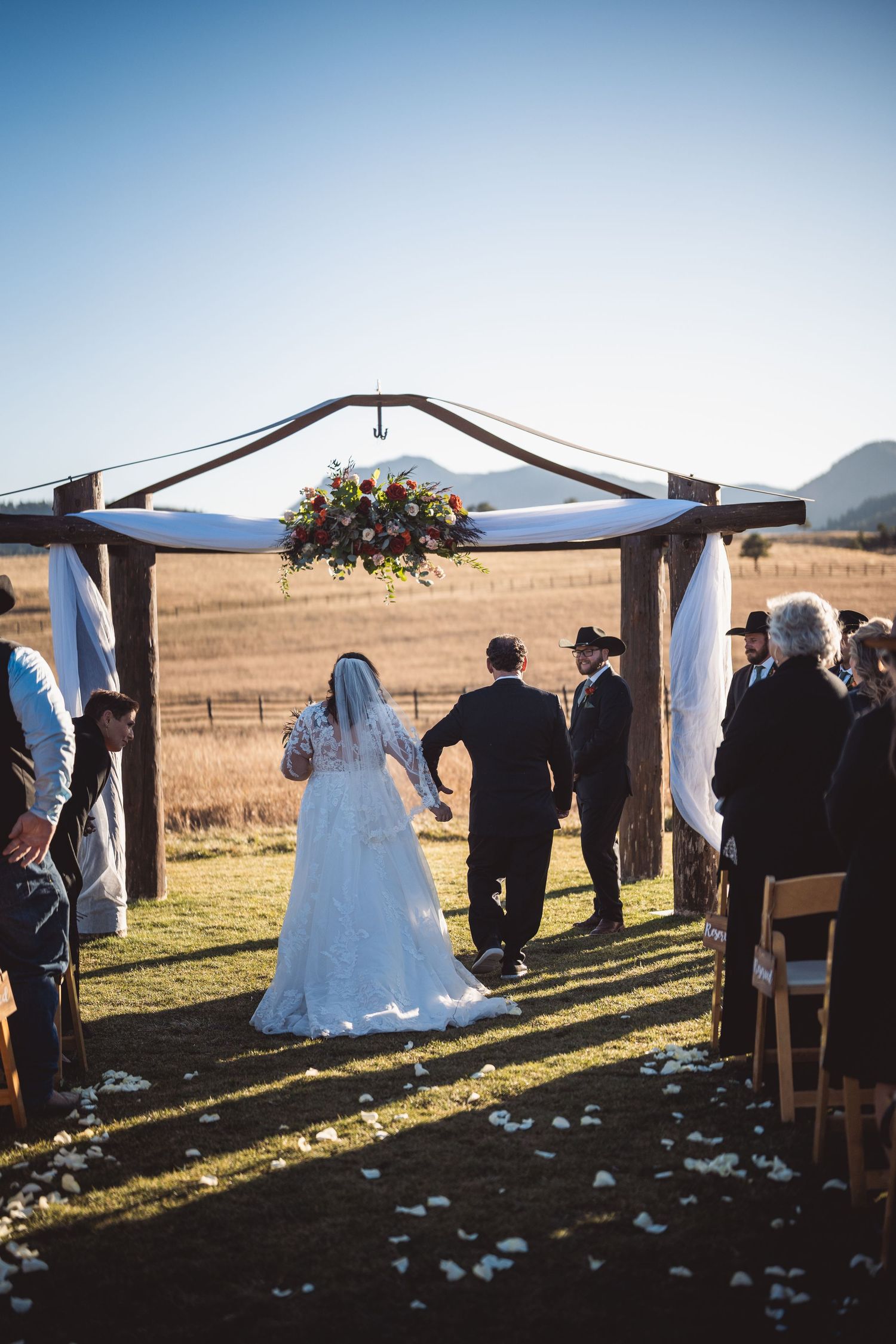 Outdoor wedding ceremony setup with white draped canopy and guest seating in a mountain landscape.
