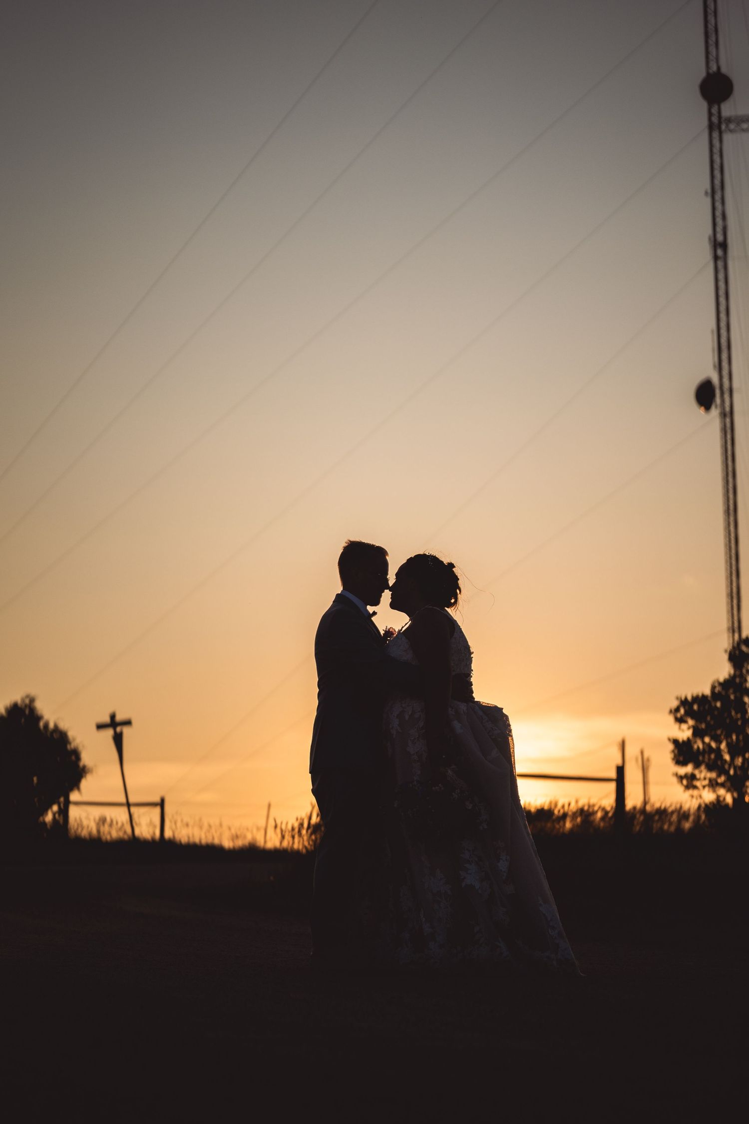 Dramatic silhouettes of wedding couple against vibrant orange sunset sky.
