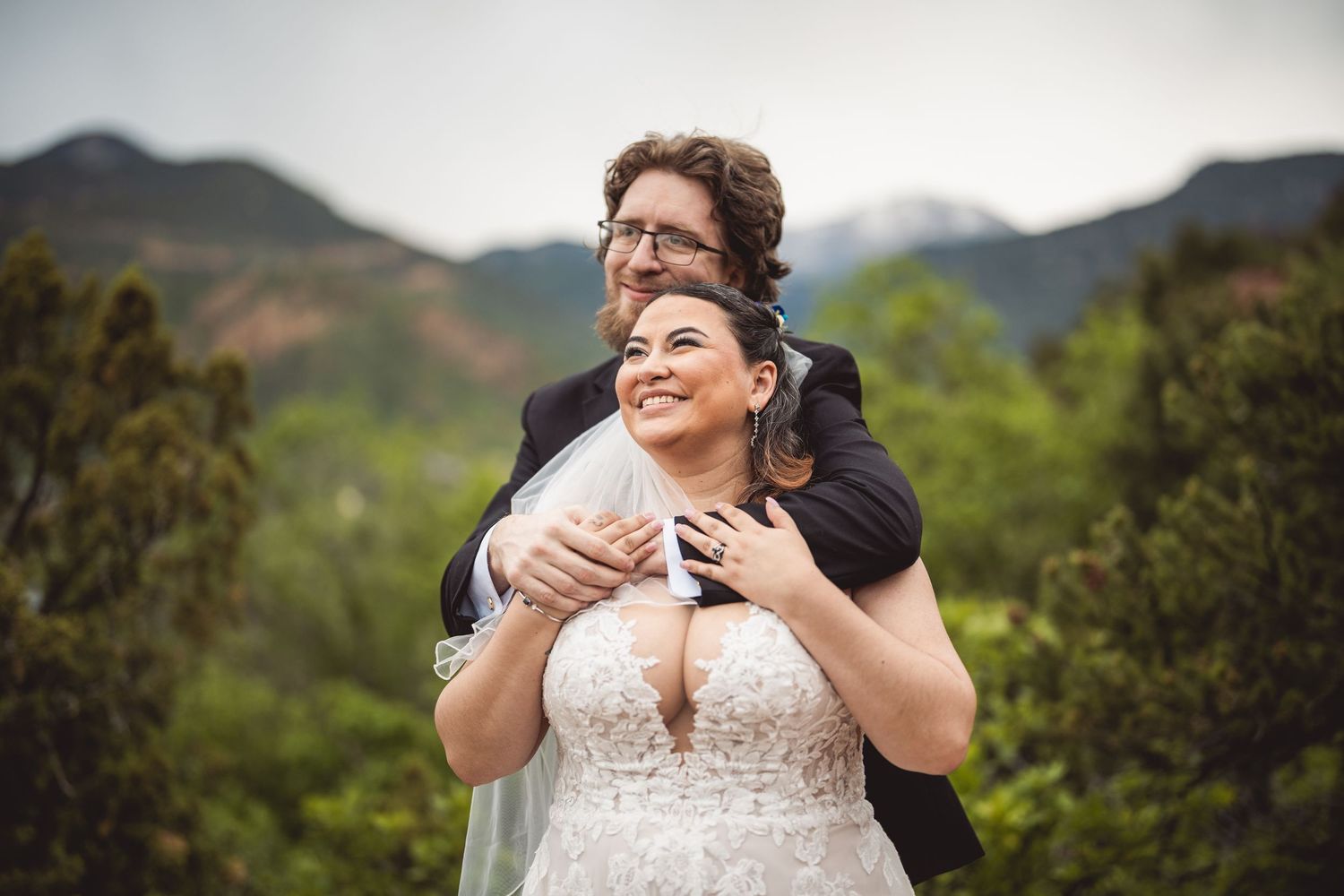A joyful wedding portrait captured against a mountainous backdrop in natural light.