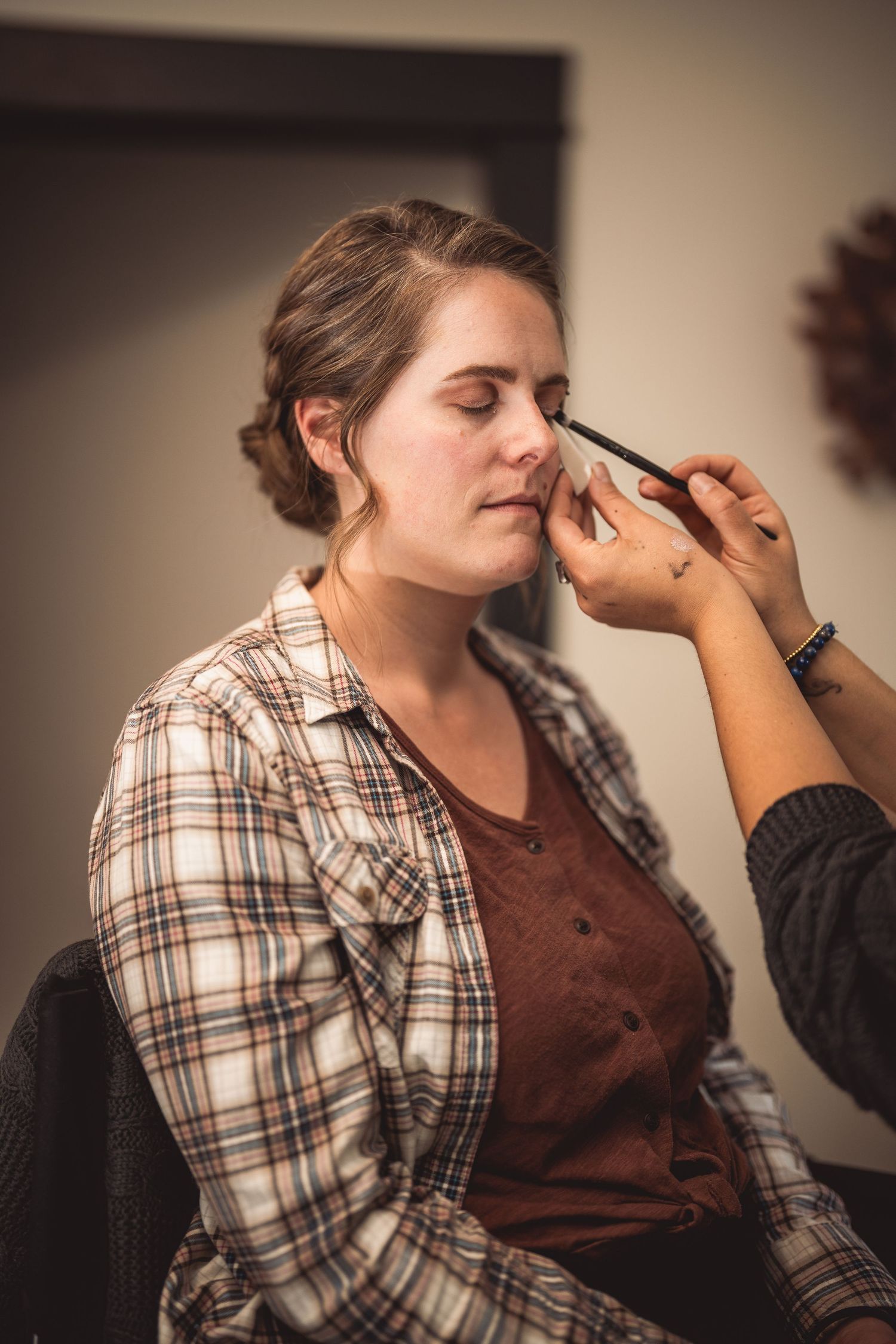 Makeup artist applying eye makeup to client in warm indoor lighting.